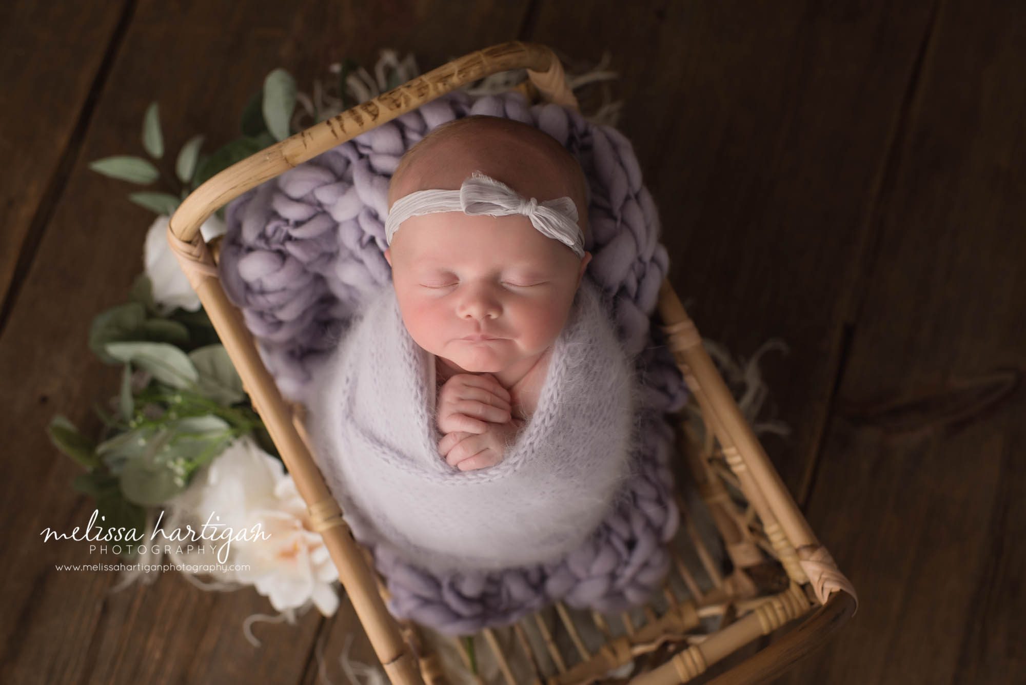 newborn baby girl wrapped in light purple posed in basket wearing newborn headband in purple