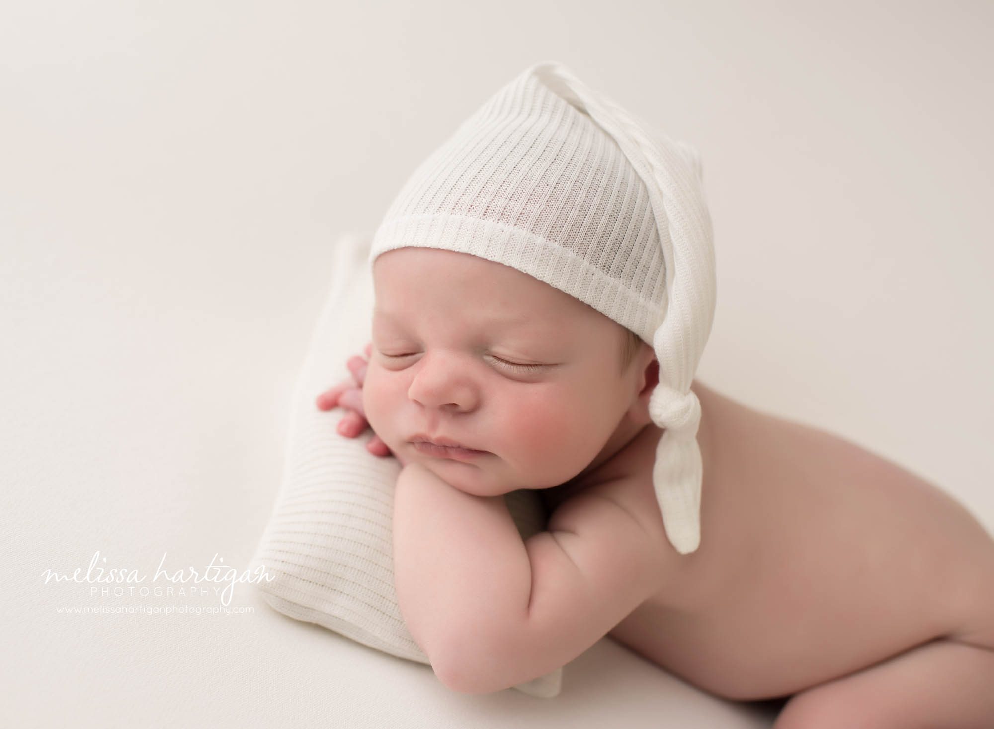 newborn baby boy posed with head on hands wearing cream sleepy cap