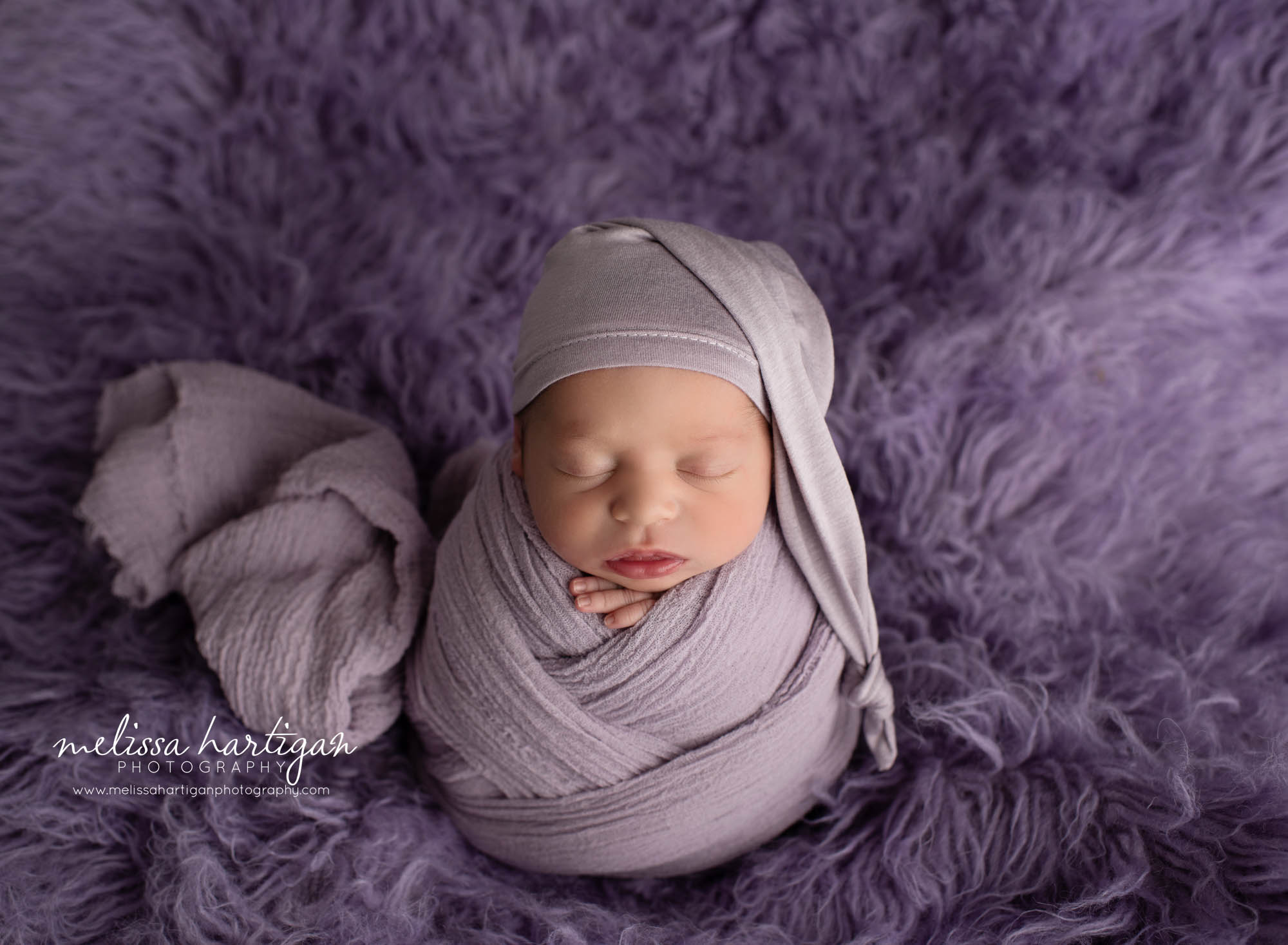 newborn baby girl posed on purple flokati rug wrapped in light purple wearing purple sleepy cap