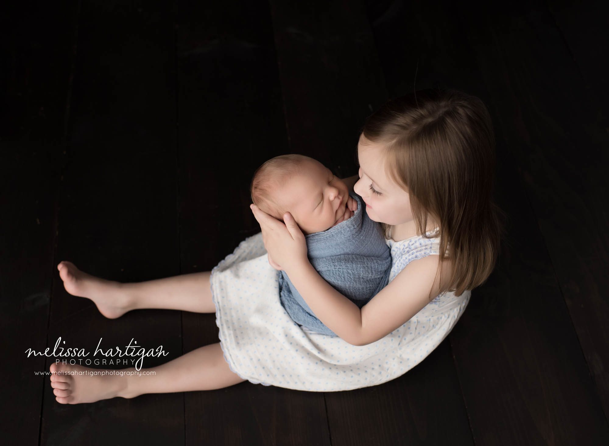 big sister holding newborn baby brother looking at him sibling pose studio newborn photography