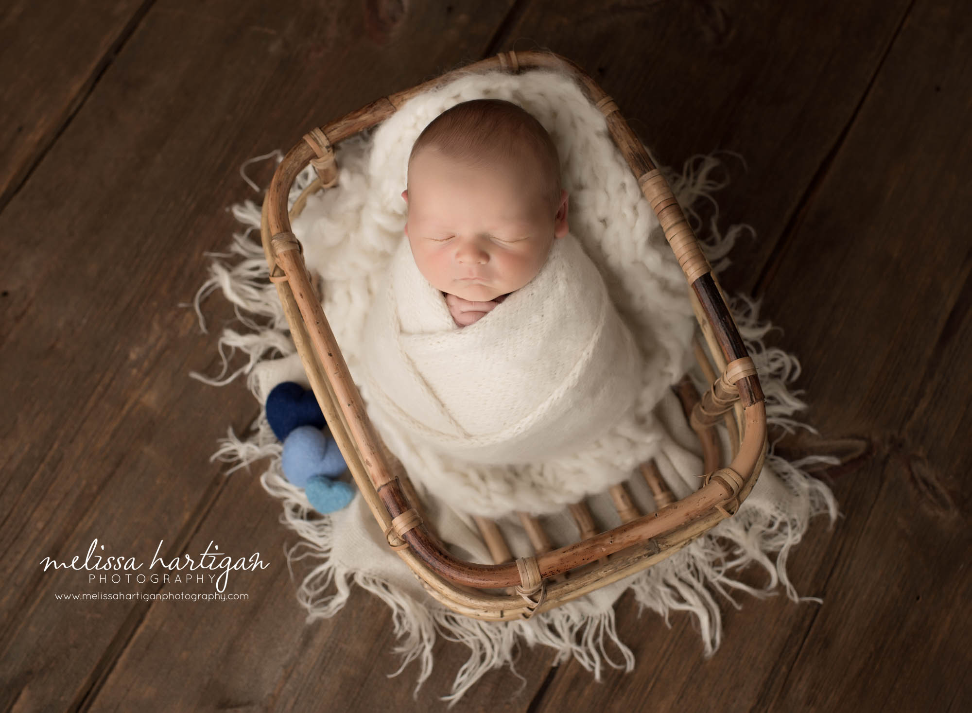 newborn baby boy wrapped in cream wrap oposed in basket with blue felted heart props newborn photographer wethersfield CT