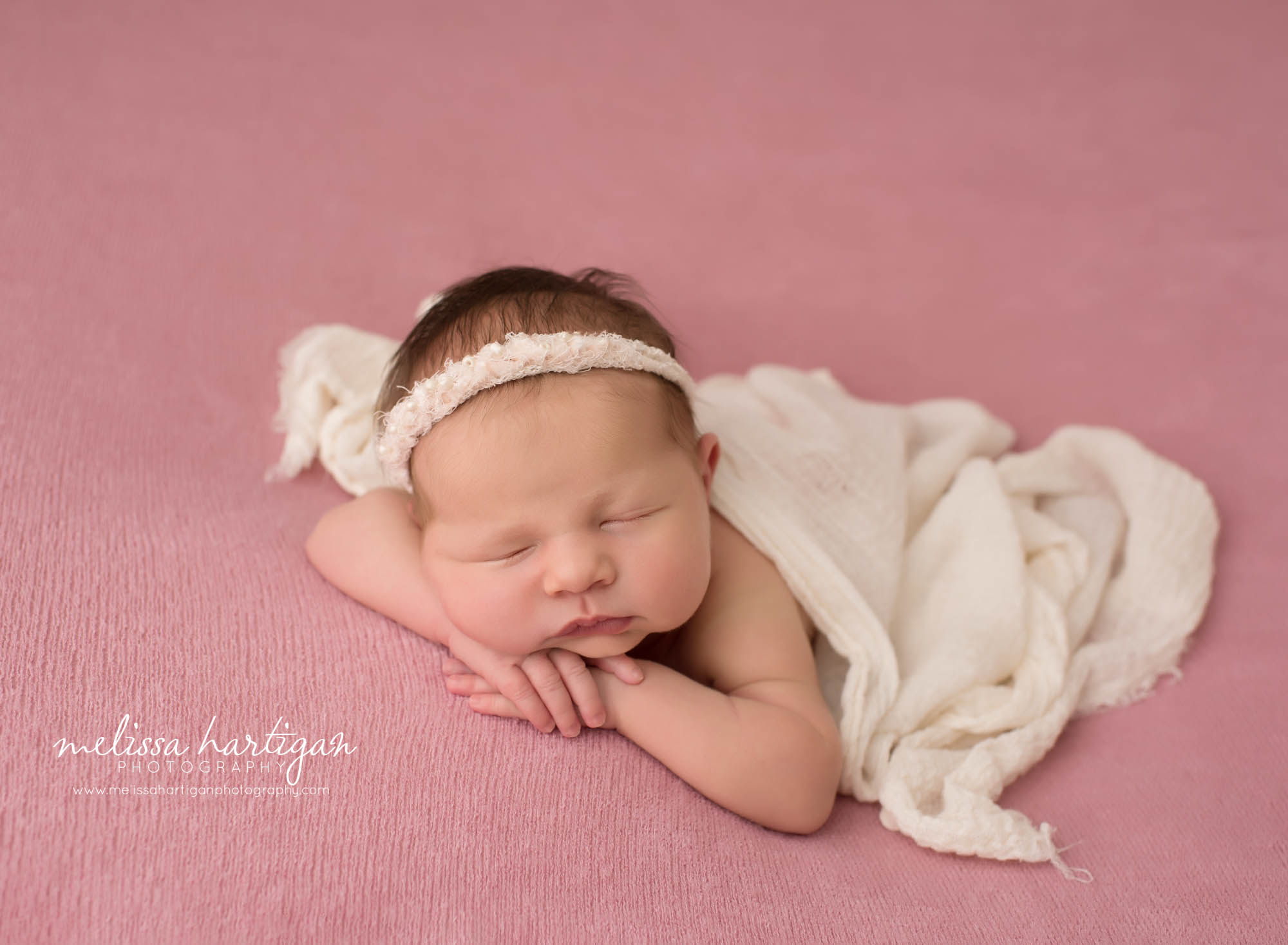 newborn baby girl posed on tummy with hands under chin wearing cream headband and cream draping wrap CT newborn photography new london county