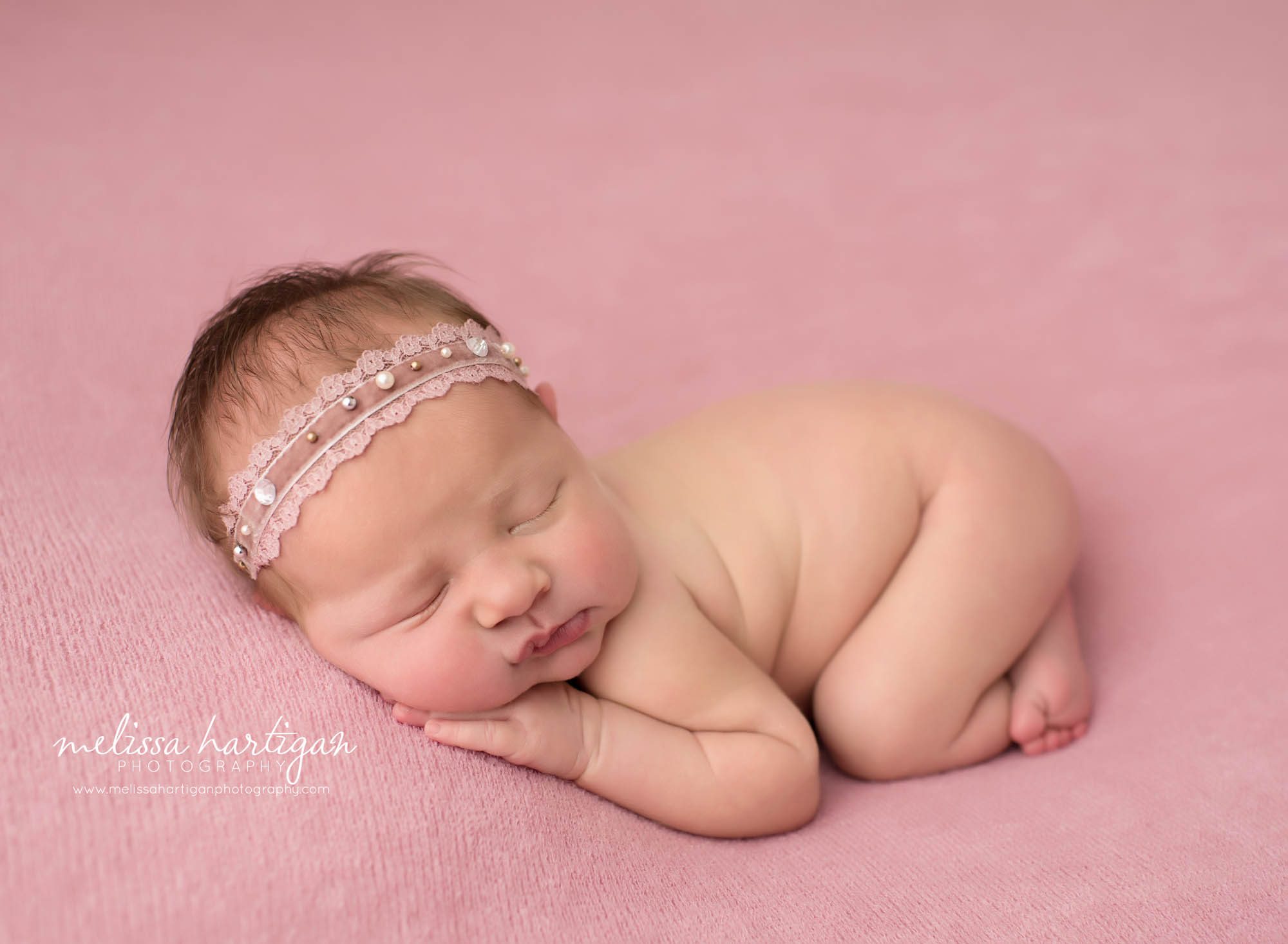 newborn baby girl posed in pink backdrop wearing pearl headband