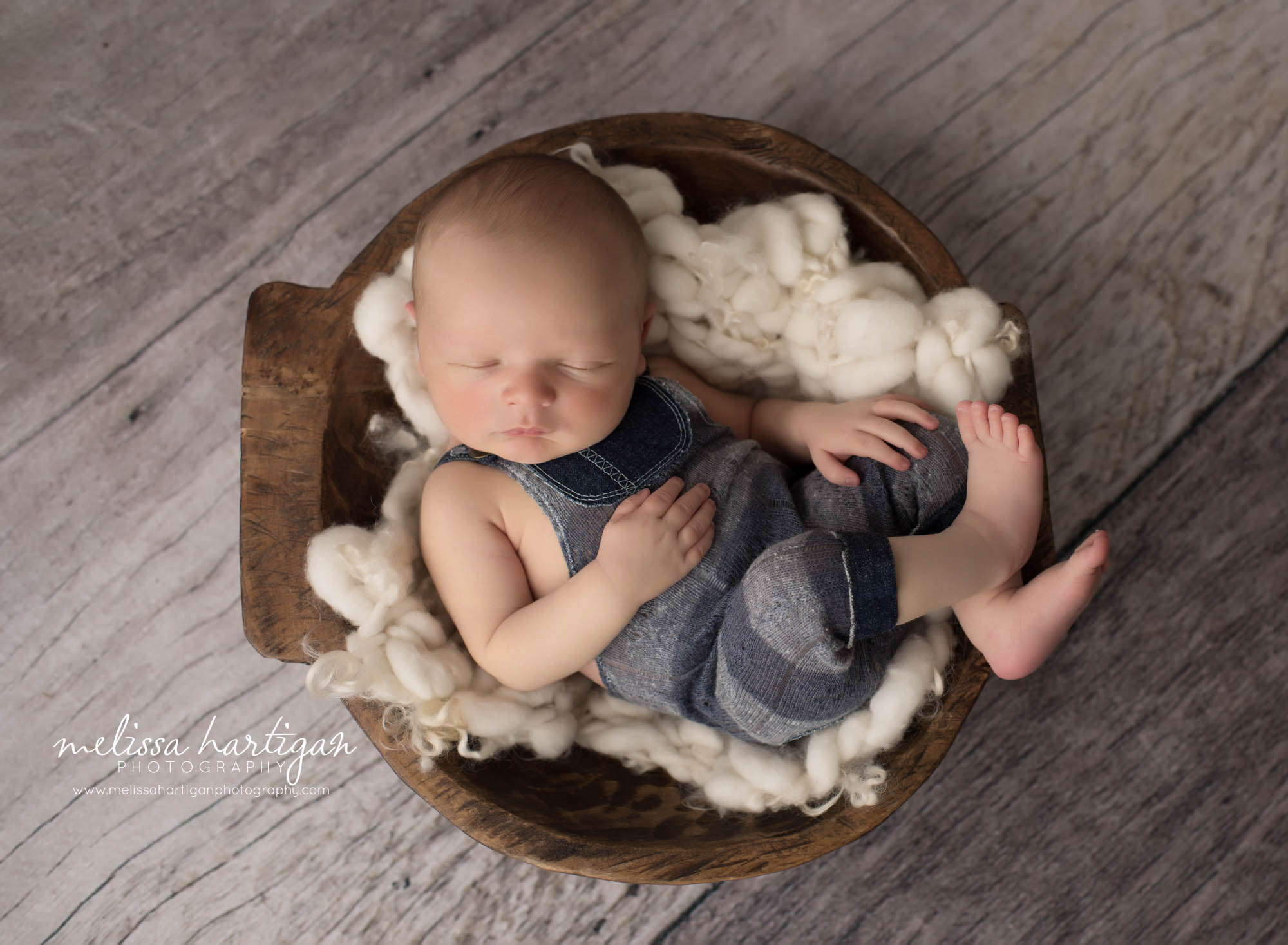 newborn baby boy wearing outfit and posed in wooden bowl with cream fluff