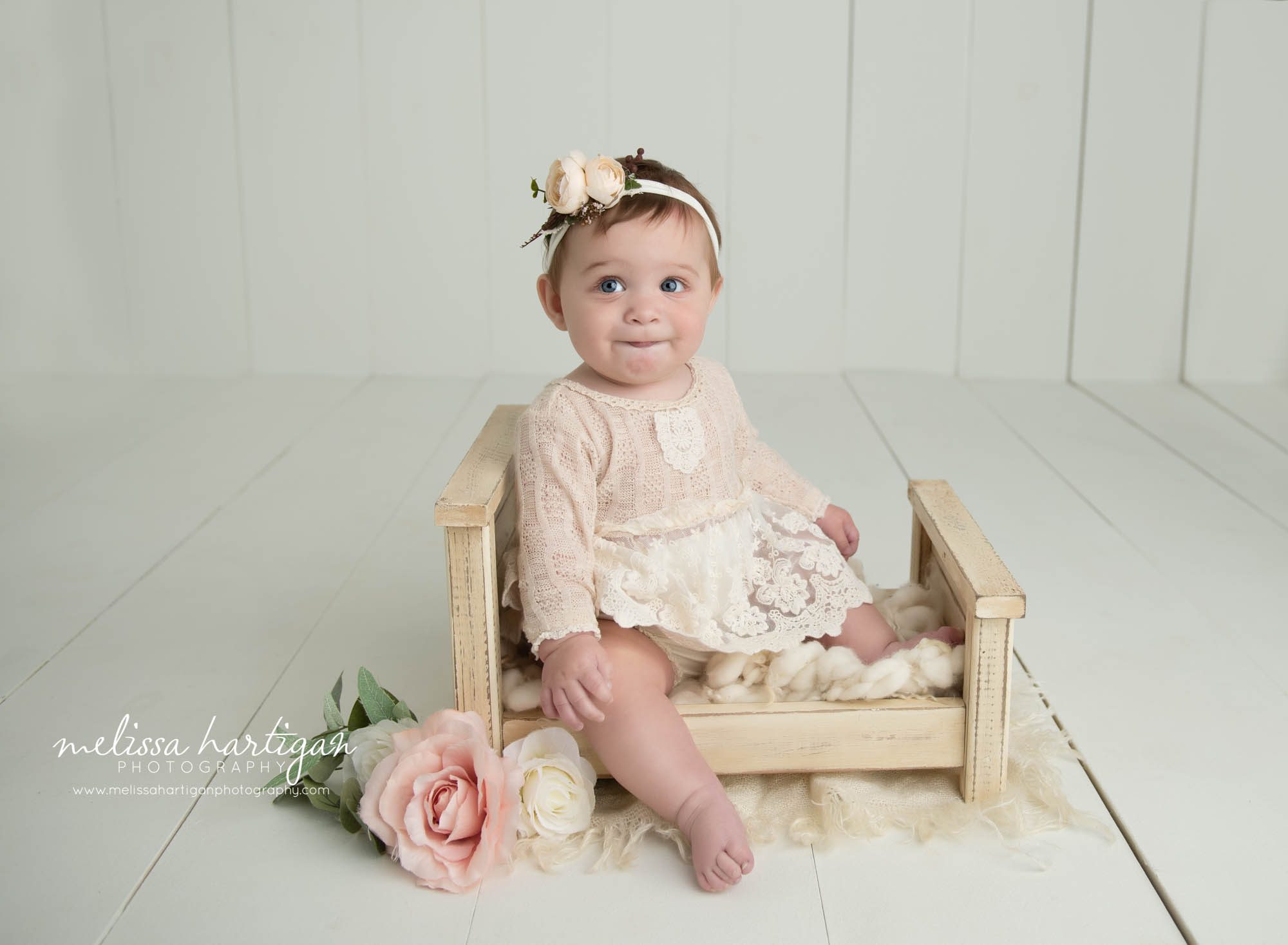 baby girl sitting on wooden bed prop wearing dream with lace on it