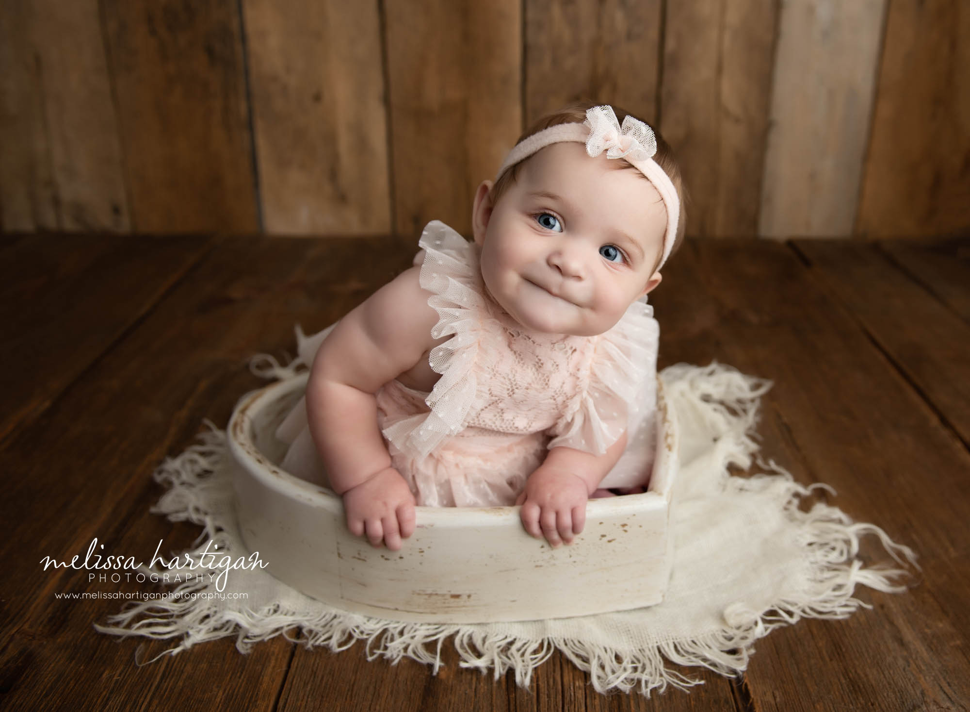 baby girl sit5ting in wooden heart prop leaning to side looking curiously tolland county CT baby photography