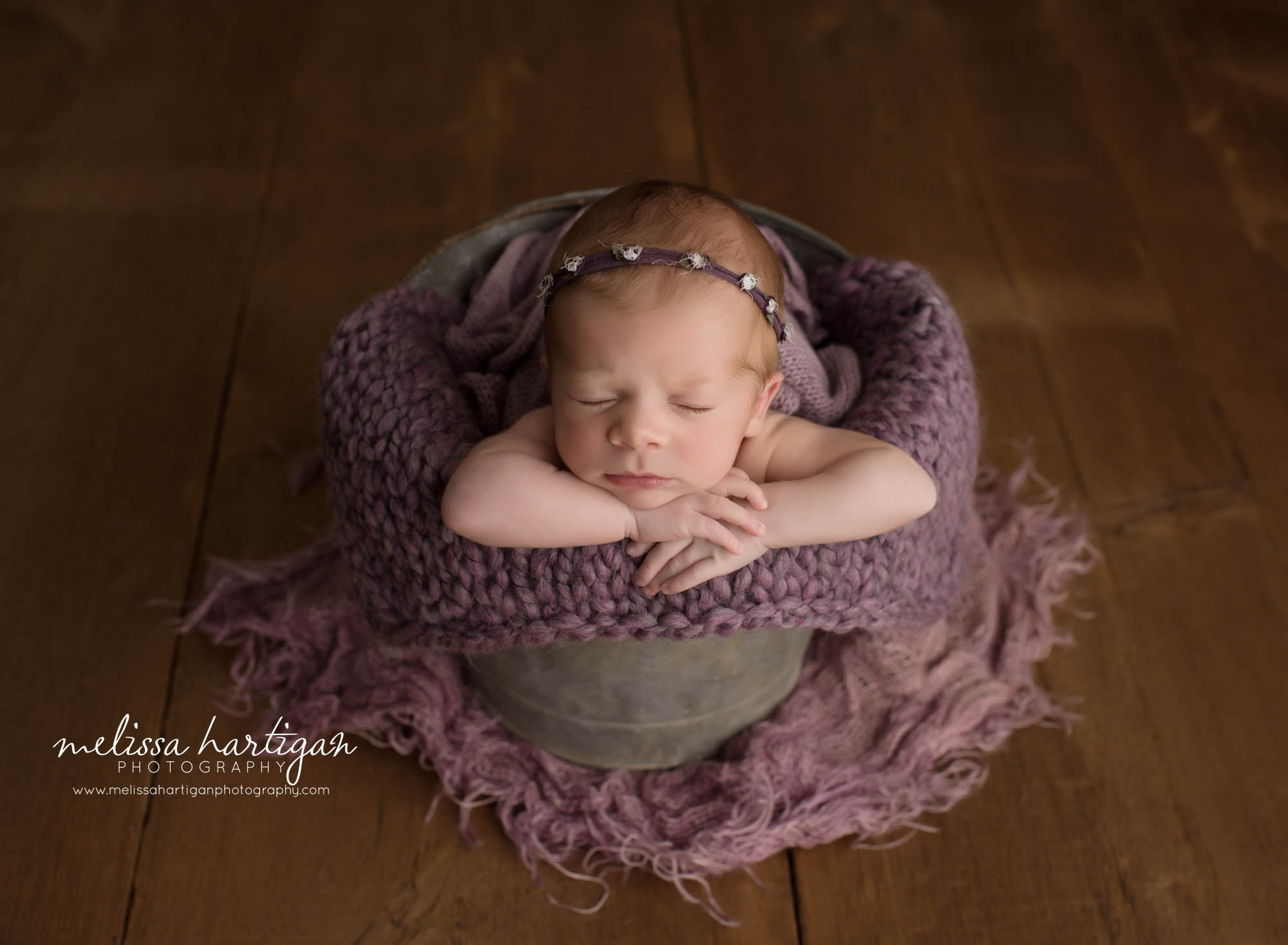 newborn baby girl posed in bucket wearing purple flower headband