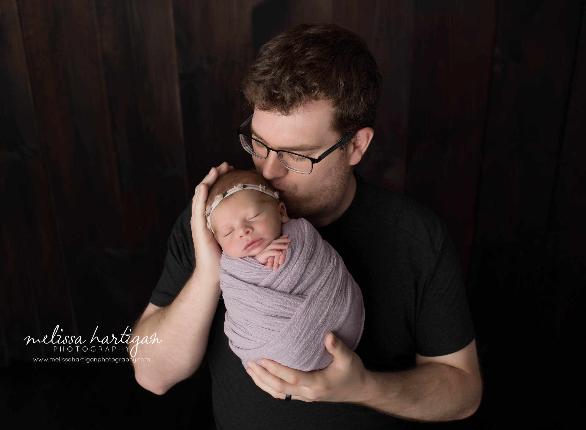dad holding newborn daughter swaddled parent pose newborn photography giving her a kiss on the forehead