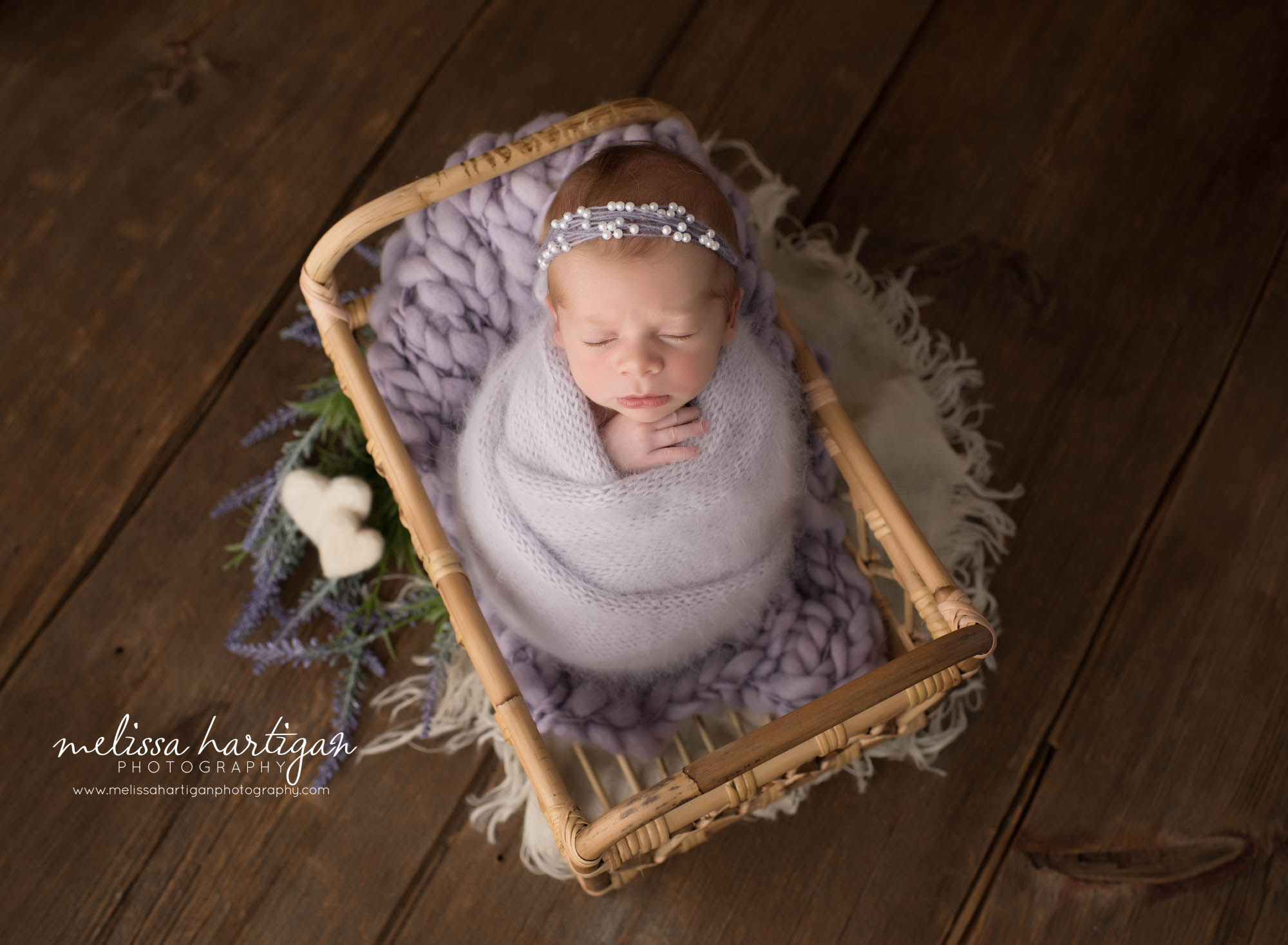 newborn baby girl posed in basket wrapped in light purple knitted wrap with purple beaded headband and white heart felted props west hartford newborn photography
