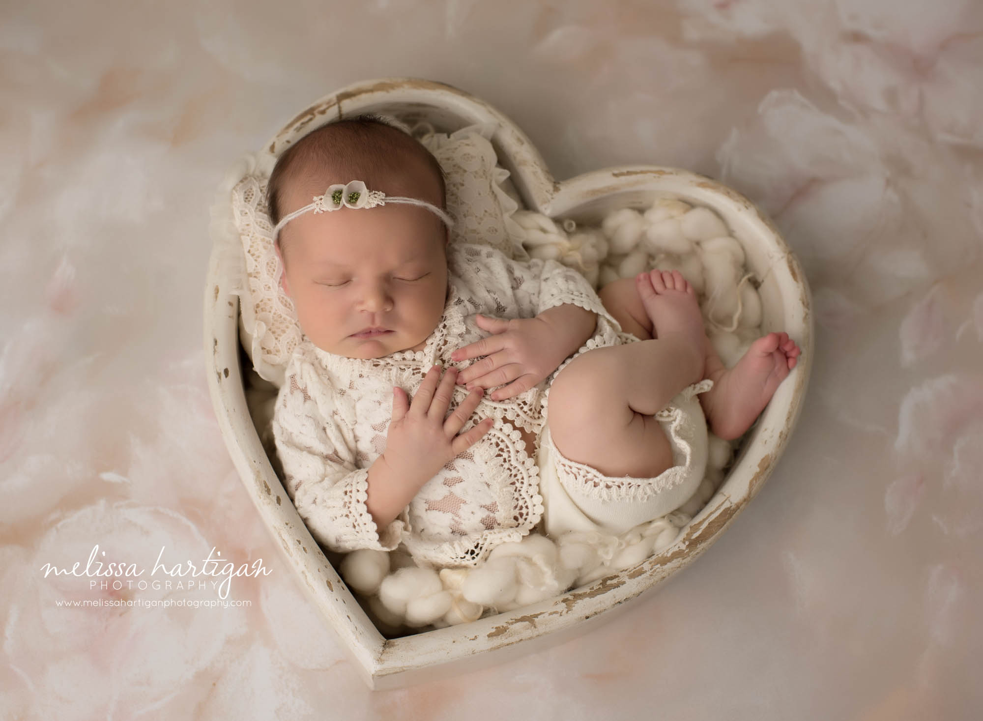 newborn baby girl posedin cream wooden heart shaped newborn photography prop wearing cream newborn girls outfit