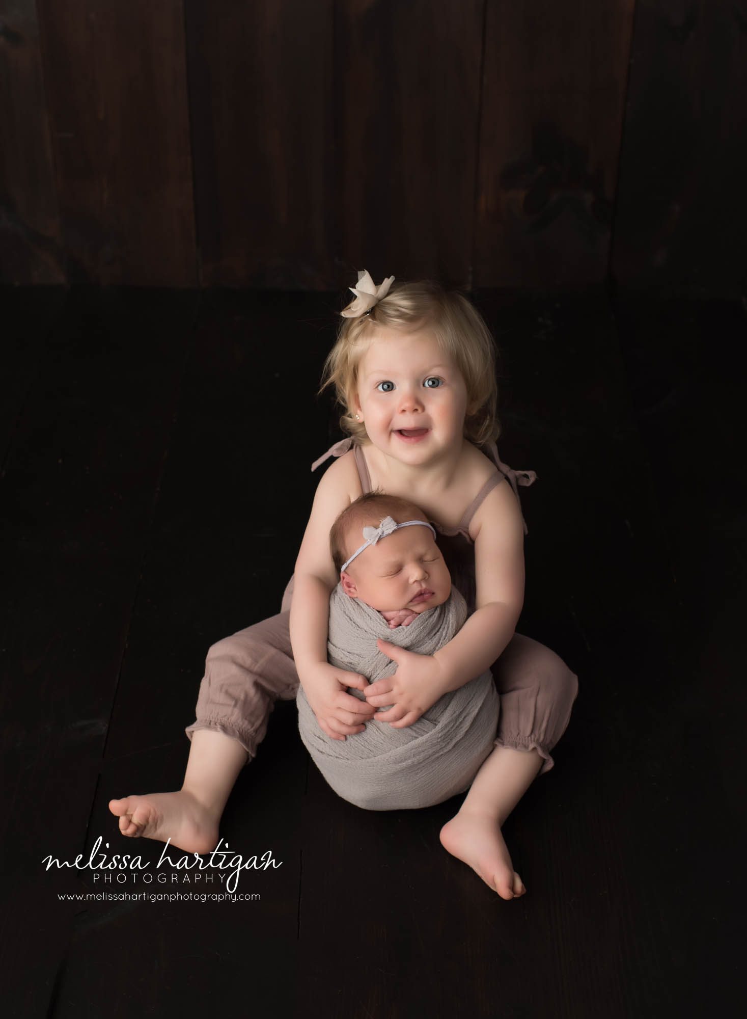 big sister holding newborn baby sister wrapped in green wrap studio newborn photographer