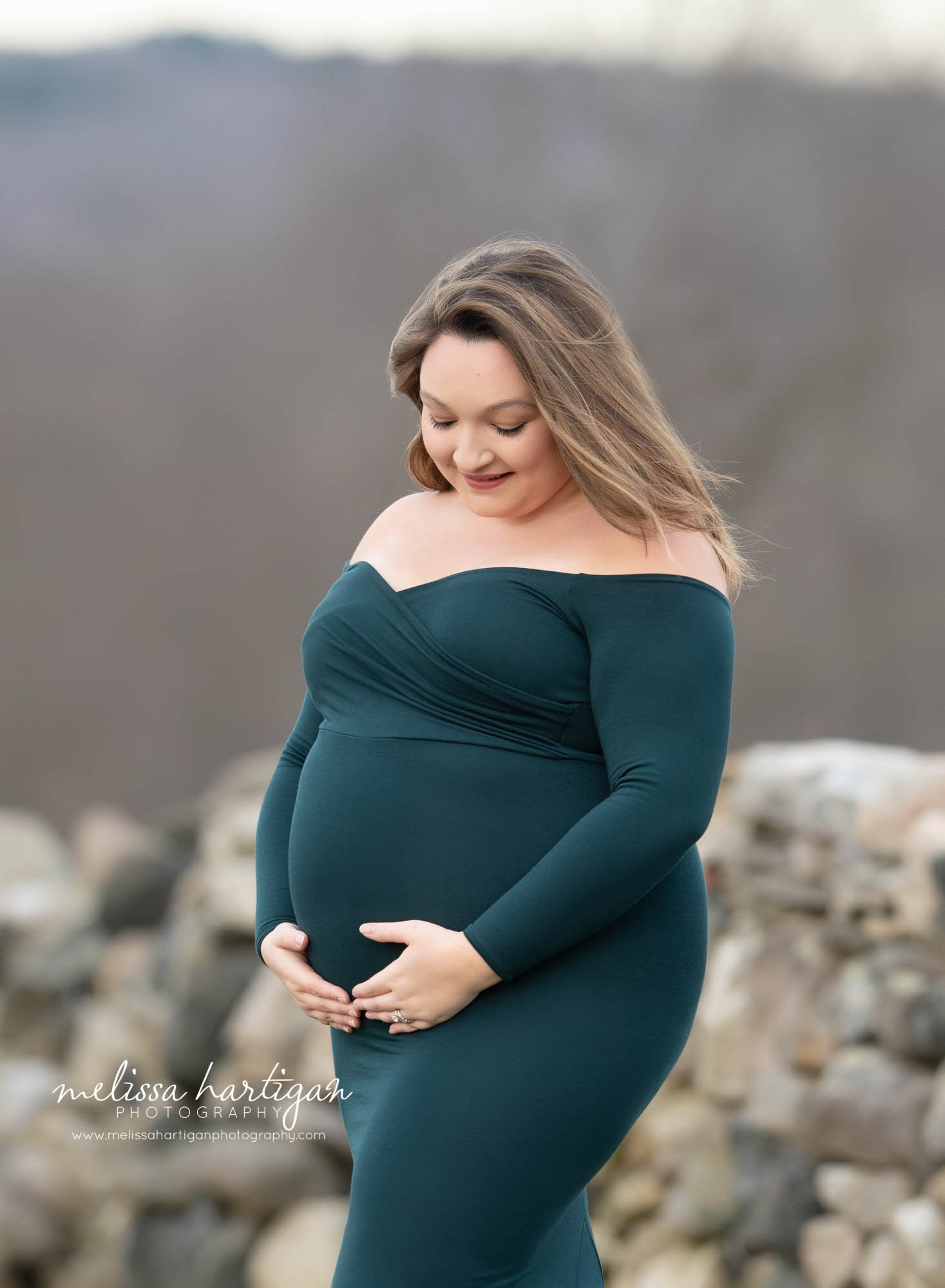 pregnant mom holding and looking down at baby bump wearing green form fitted long sleeved maternity gown maternity photography Amston CT