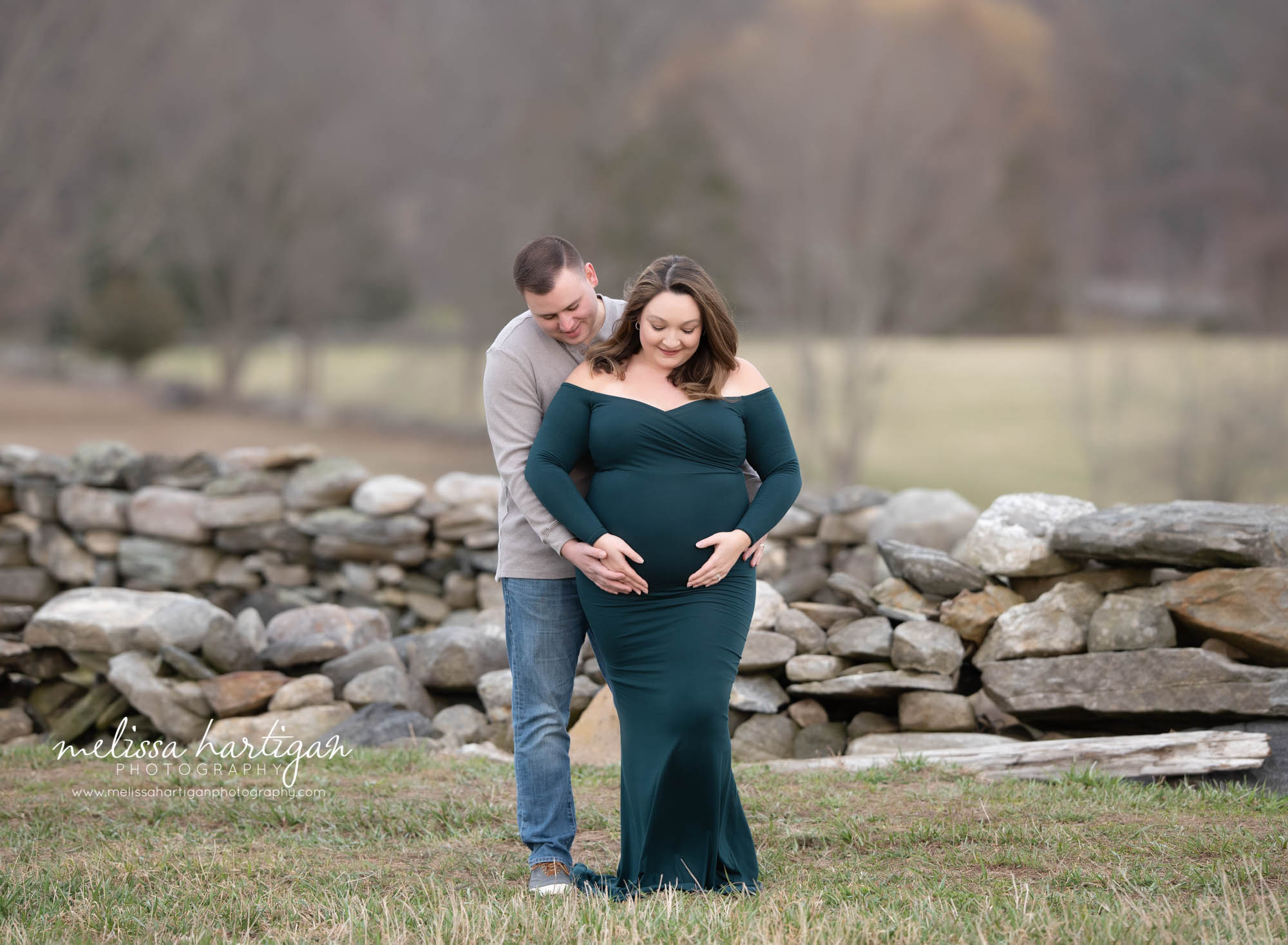 mom and dad to be standing holding baby bump looking down at baby belly maternity photographer Amston CT