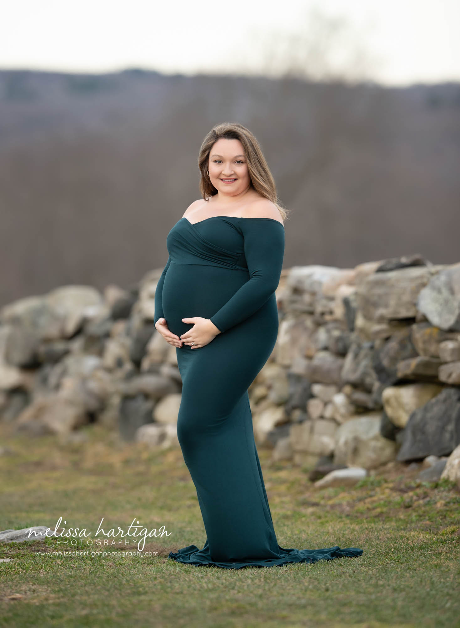 expectant mom standing holding baby belly smiling happy wearing green form fitted maternity gown