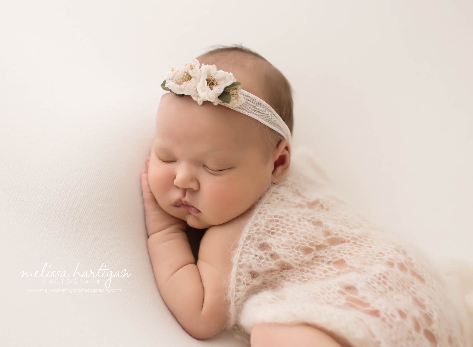 newborn baby girl posed on side with knitted layer draped over back hand under cheek wearing floral headband newborn photographer CT