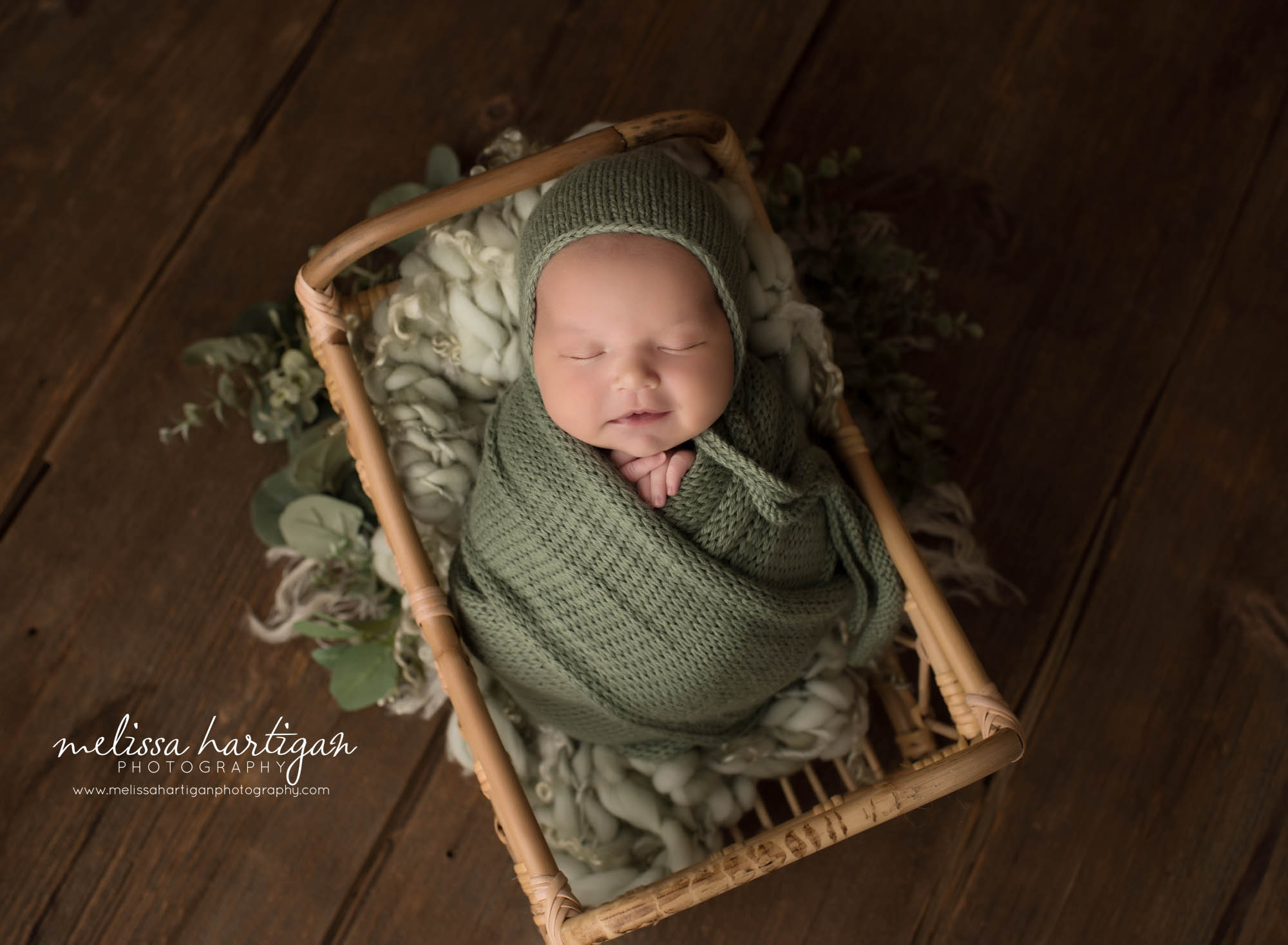 newborn baby girl wrapped in green knitted wrap posed in basket with green curly layer newborn photography rocky hill CT