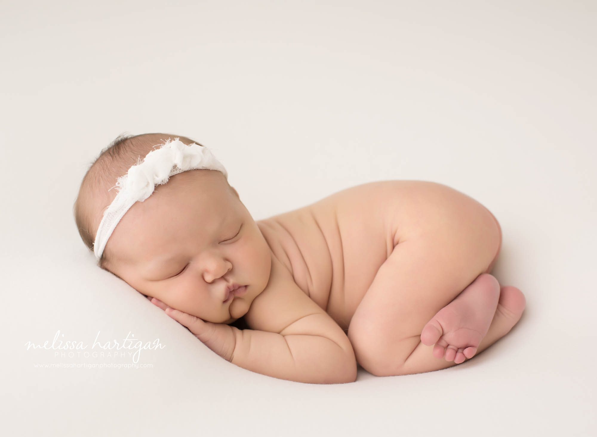 newborn baby girl posed on white backdrop wearing whit floral headband newborn photography rocky hill