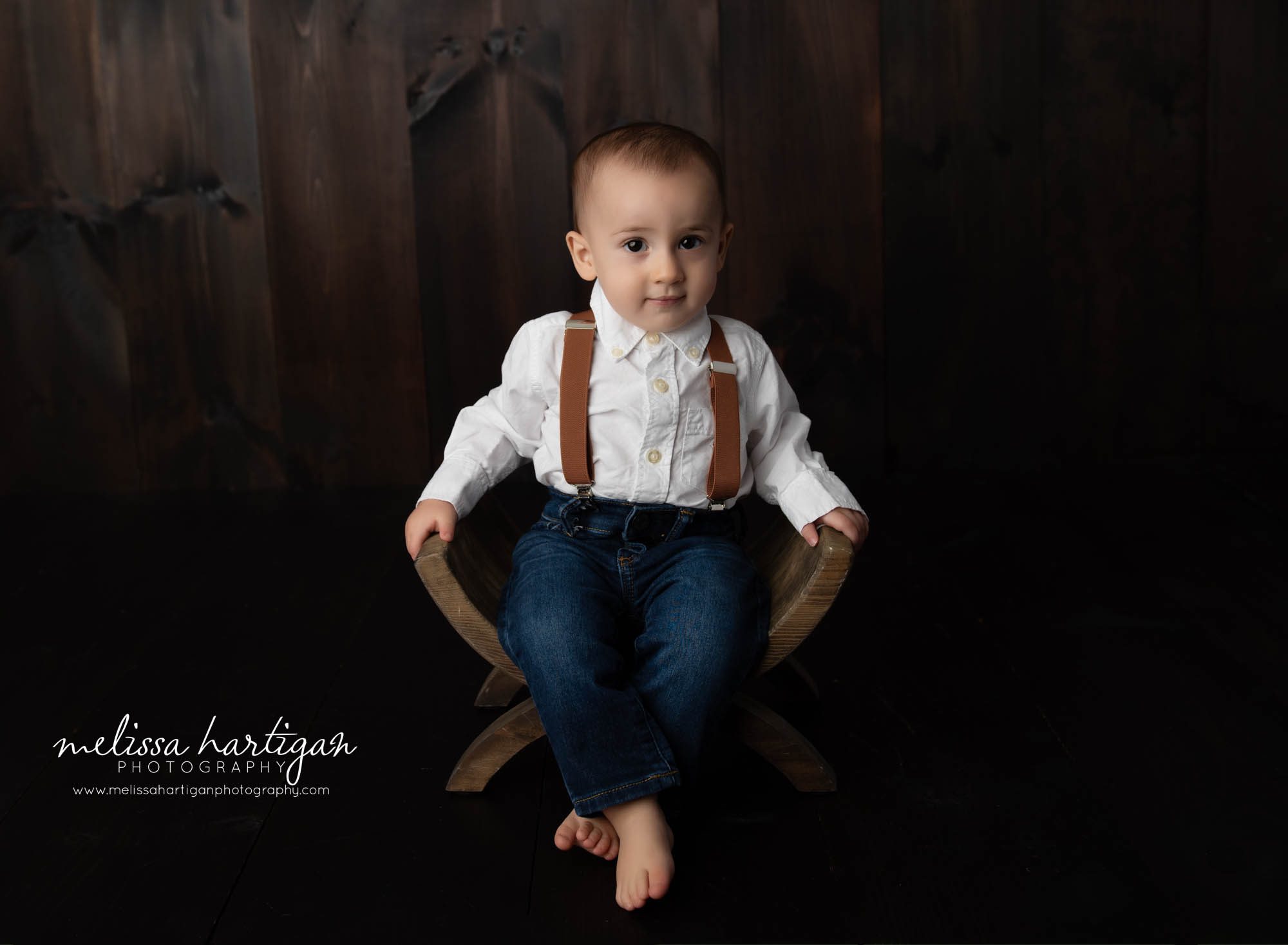 baby boy sitting on wooden U shaped prop wearing suspenders