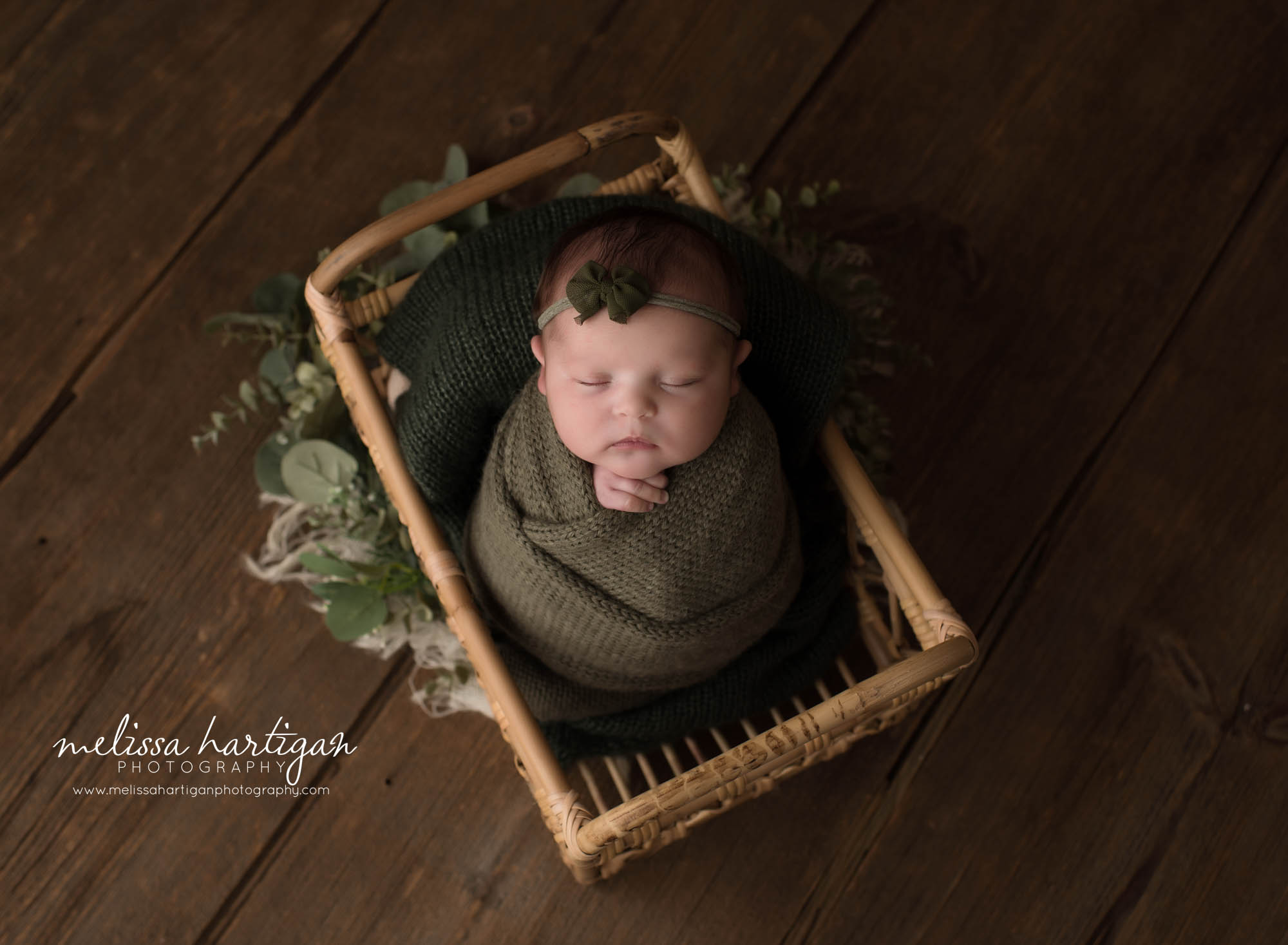 newborn baby girl posed in basket wrapped in green knitted wrap wearing green headband tieback newborn photographer