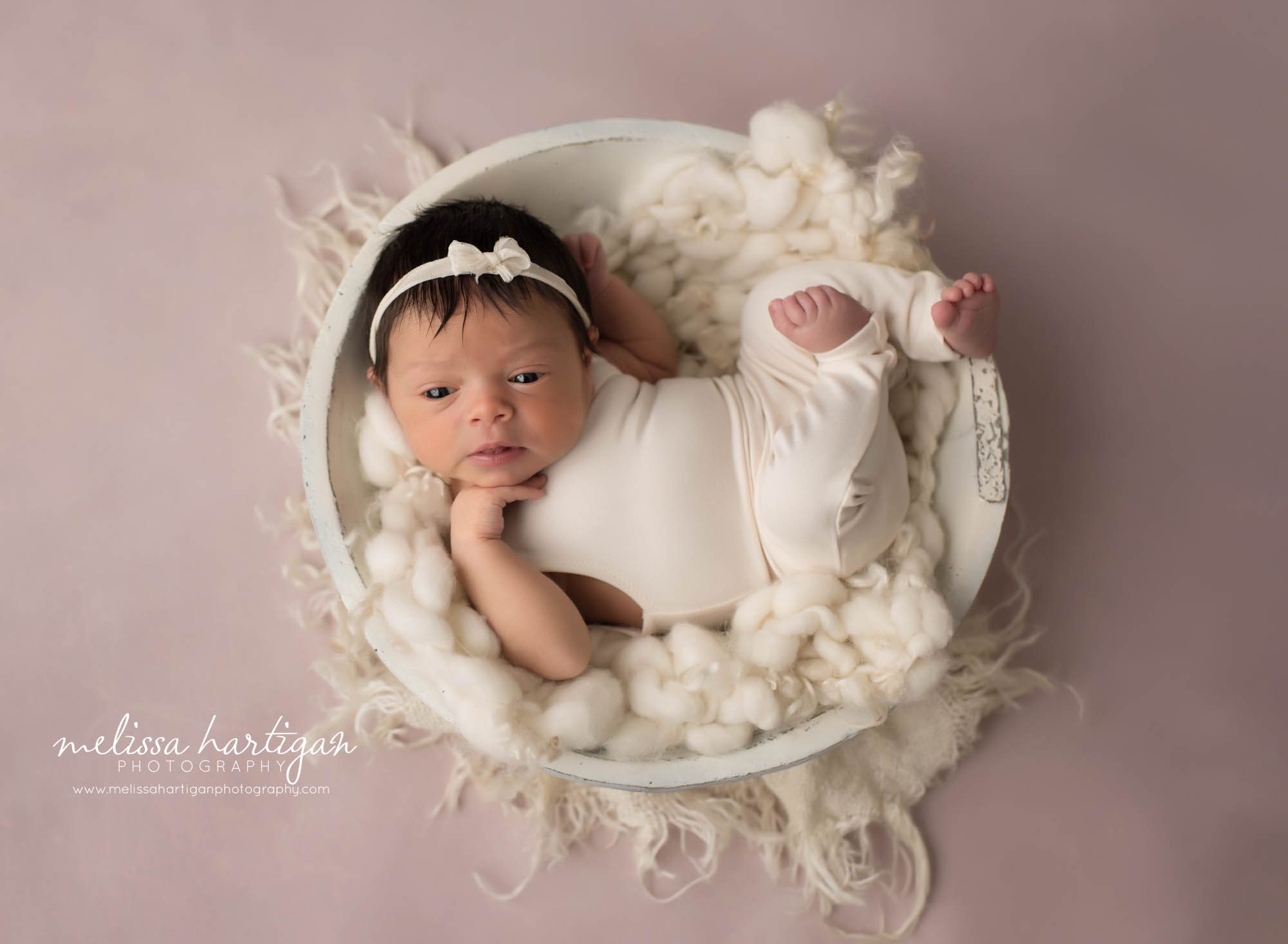 newborn baby girl wearing cream outfit posed in cream wooden bowl with cream layer fluff