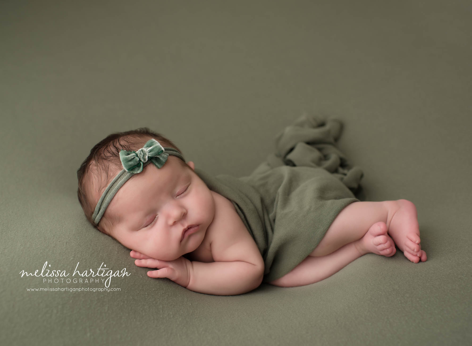 newborn baby girl posed sleeping on side tummy with hand under cheek wearing green bow headband Massachusetts maternity newbornphotography