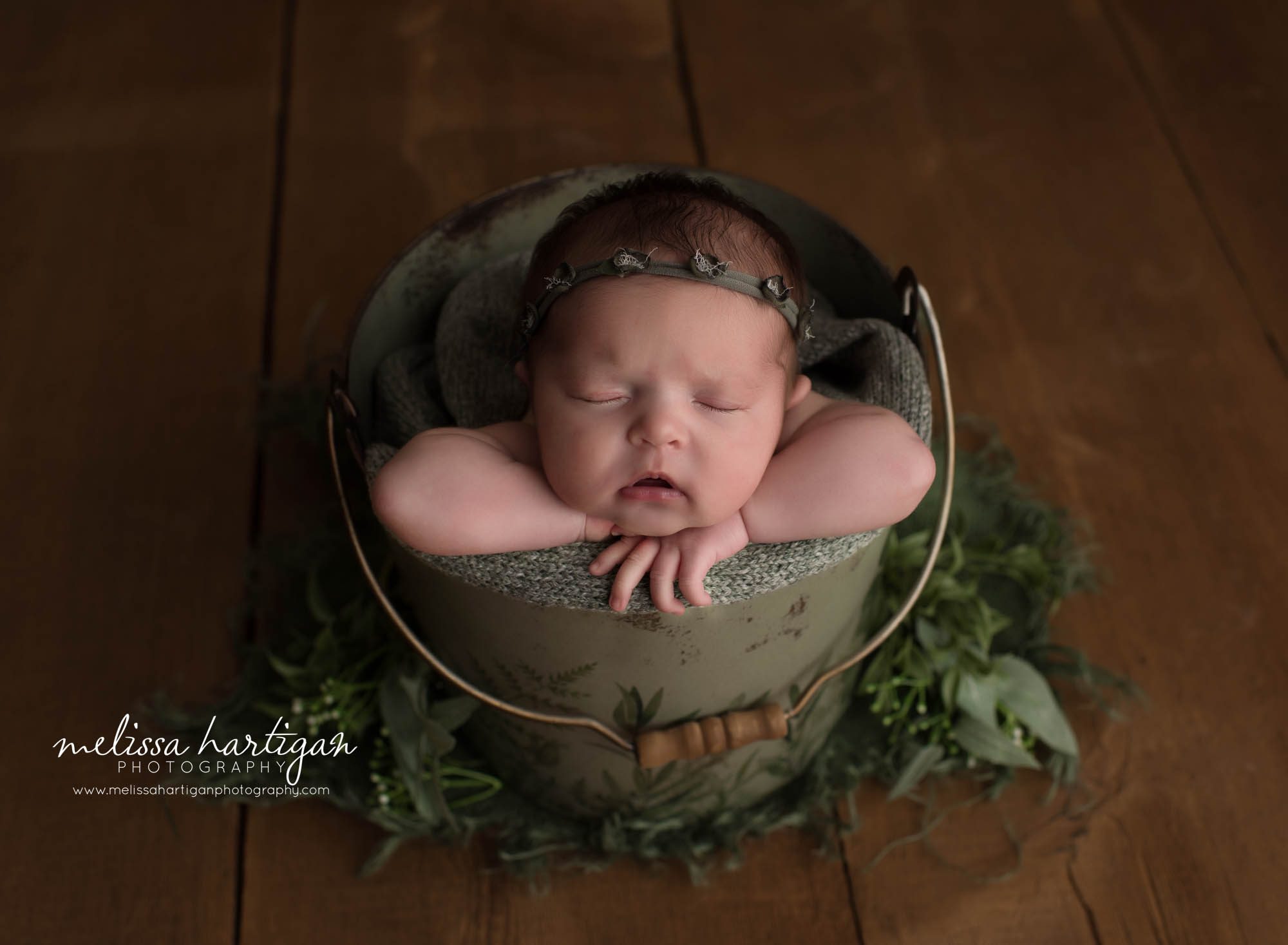 newborn baby girl posed in green metal bucket wearing green headband