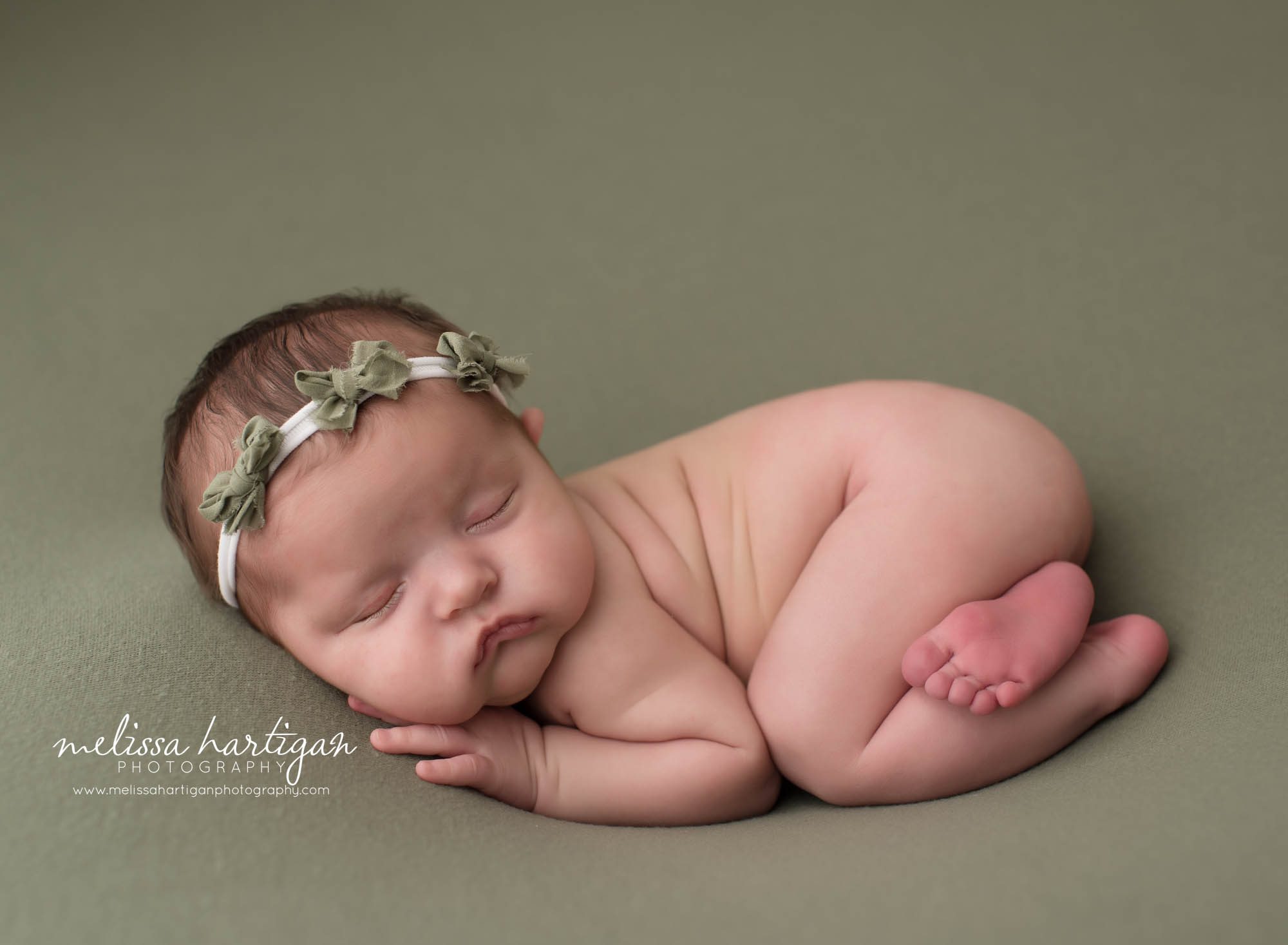 newborn baby girl posed on green backdrop wearing green bow headband
