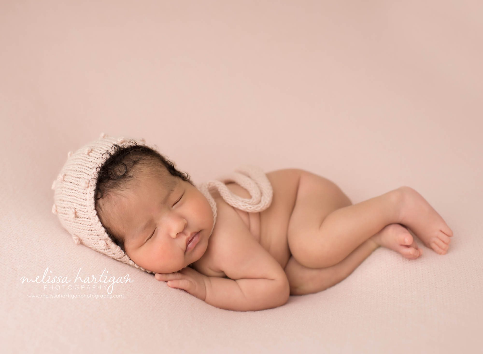 baby girl posed on pink backdrop wearing knitted pink bonnet