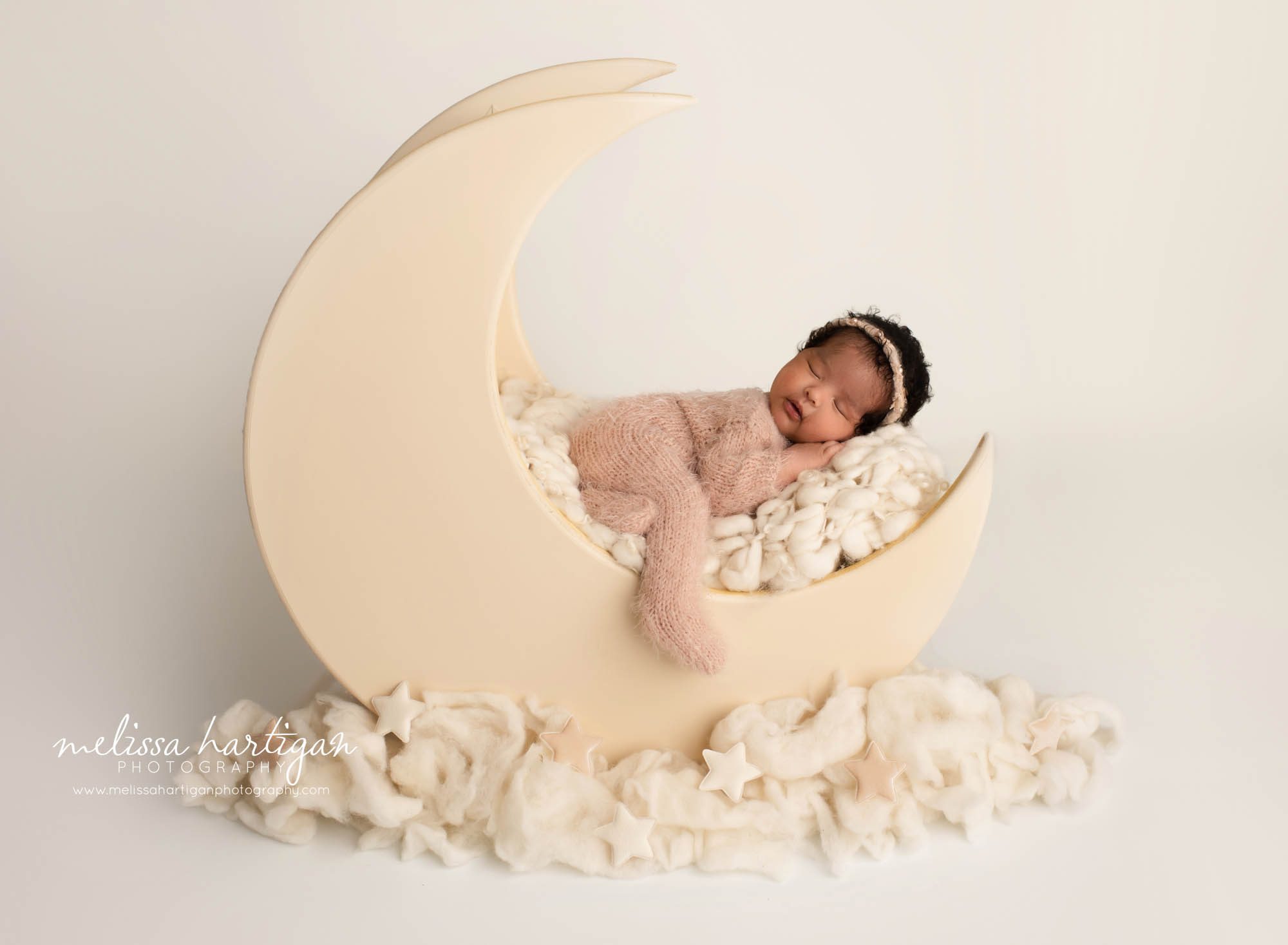 newborn baby girl posed in wooden moon prop wearing pink knitted footed sleeper