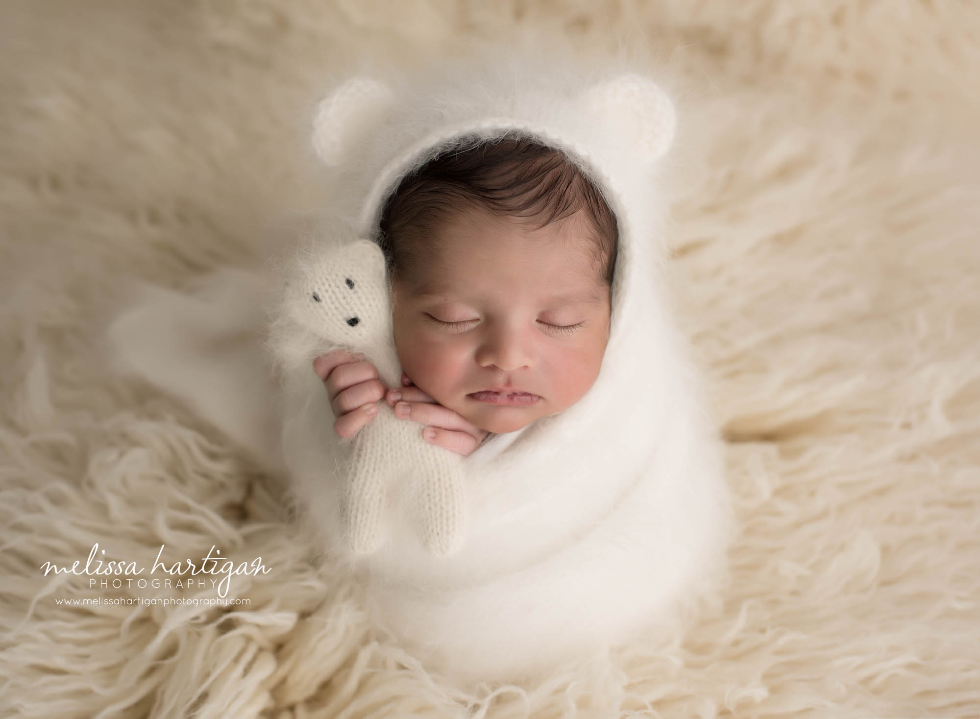 newborn baby boy posed in cream flokati wrapped in cream knitted wrap and matching bear bonnet