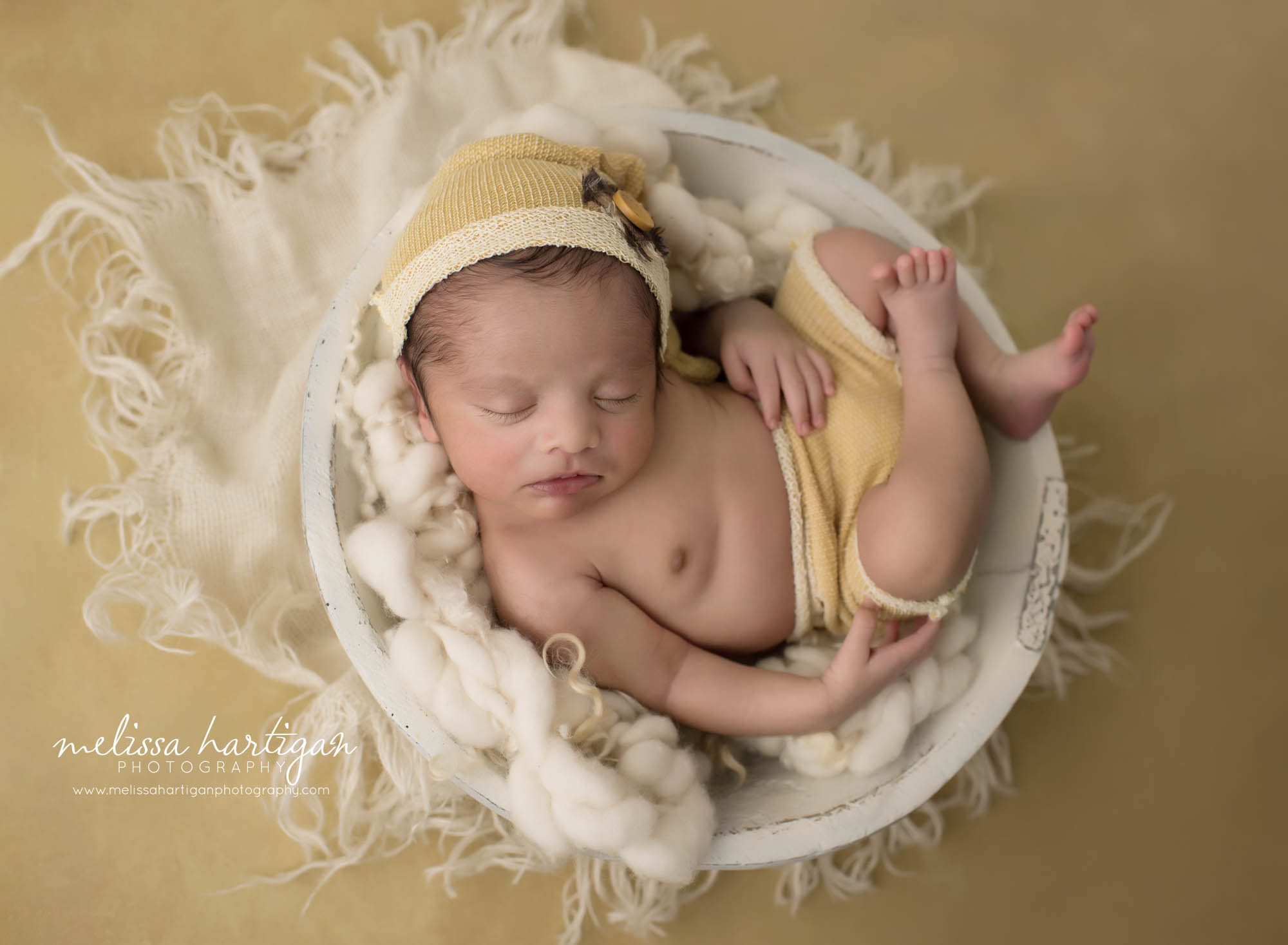 newborn baby boy posed in bowl wearing yellow sleepy cap and shorts set