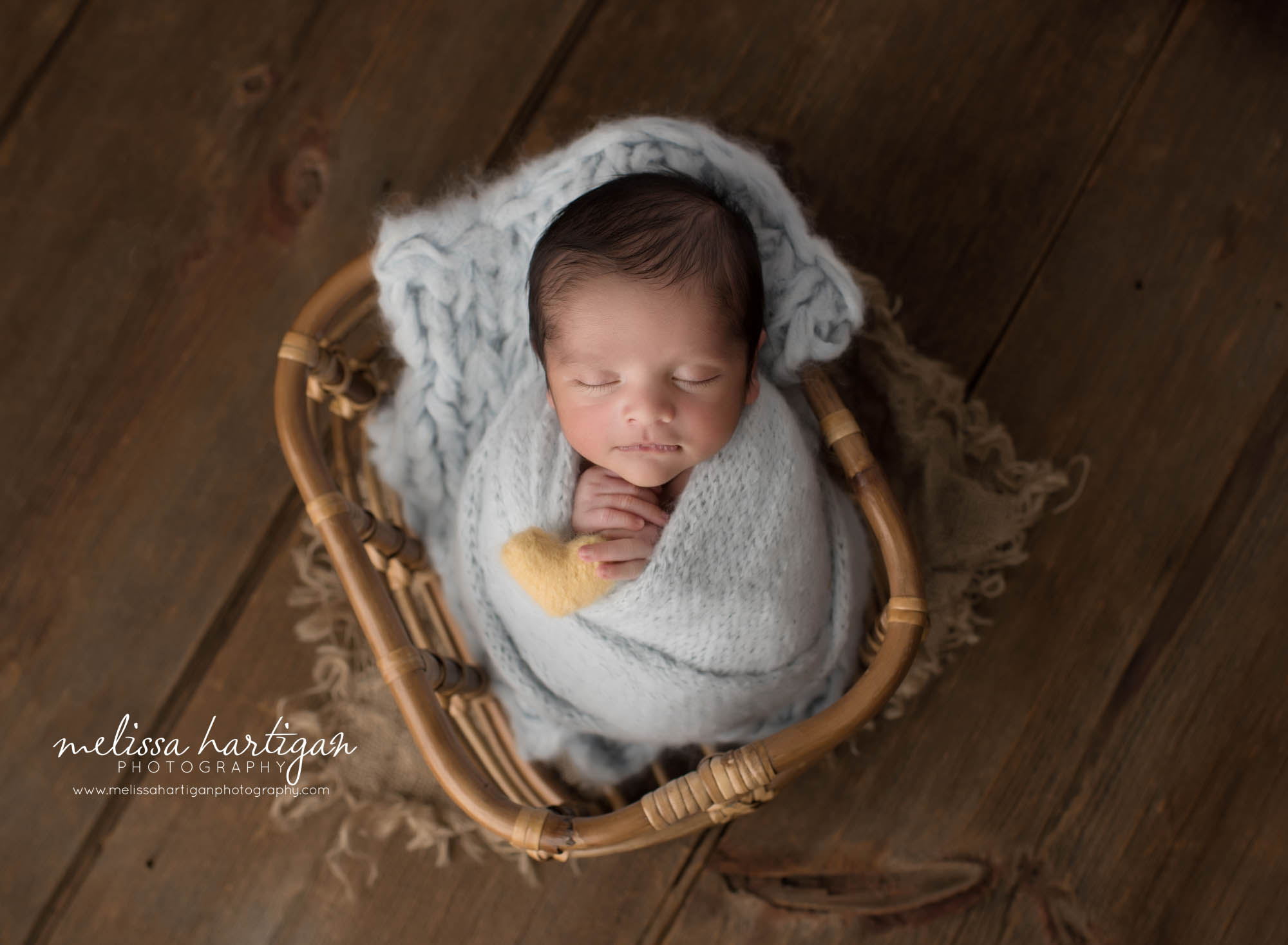 newborn baby boy wrapped in light blue wrap posed in basket holding yellow felted heart prop