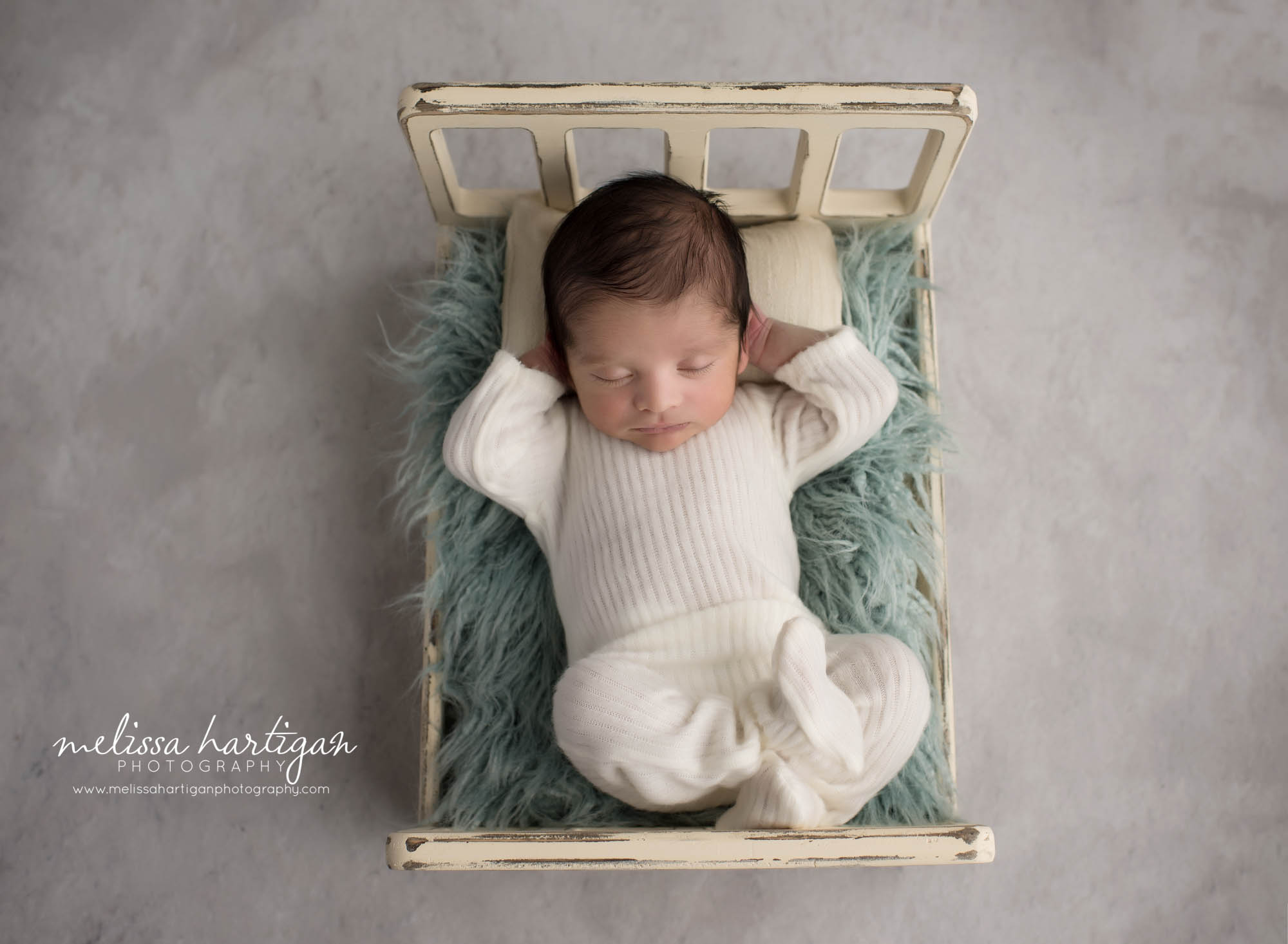 newborn baby boy posed on bed prop in relaxed baby pose sleeping