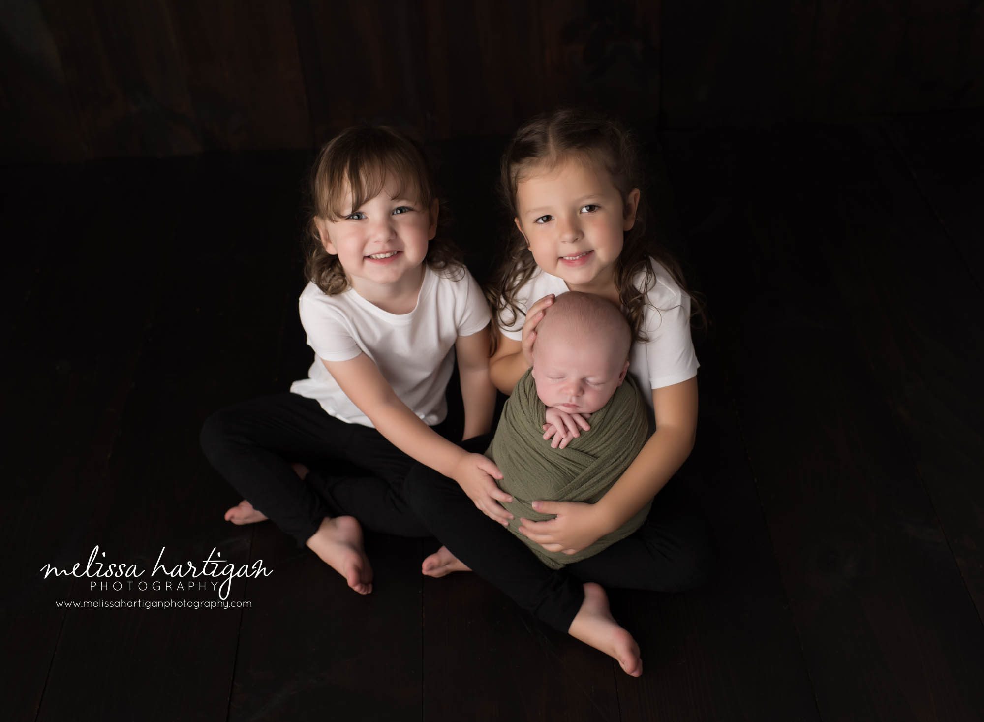 newborn baby boy wrapped and held by his two older sisters family pose
