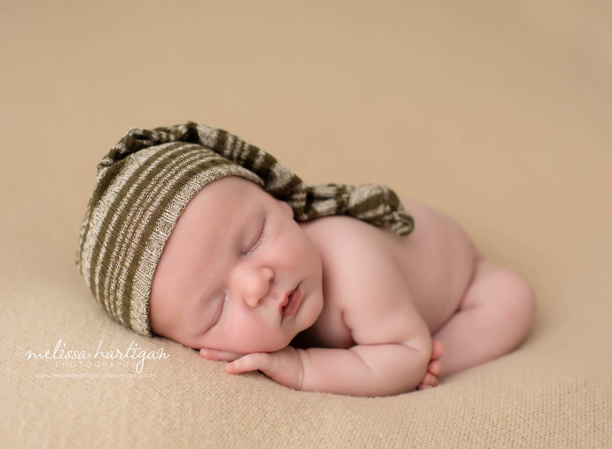newborn baby boy posed on tan backdrop wearing green stripped sleepy cap newborn photographer columbia CT