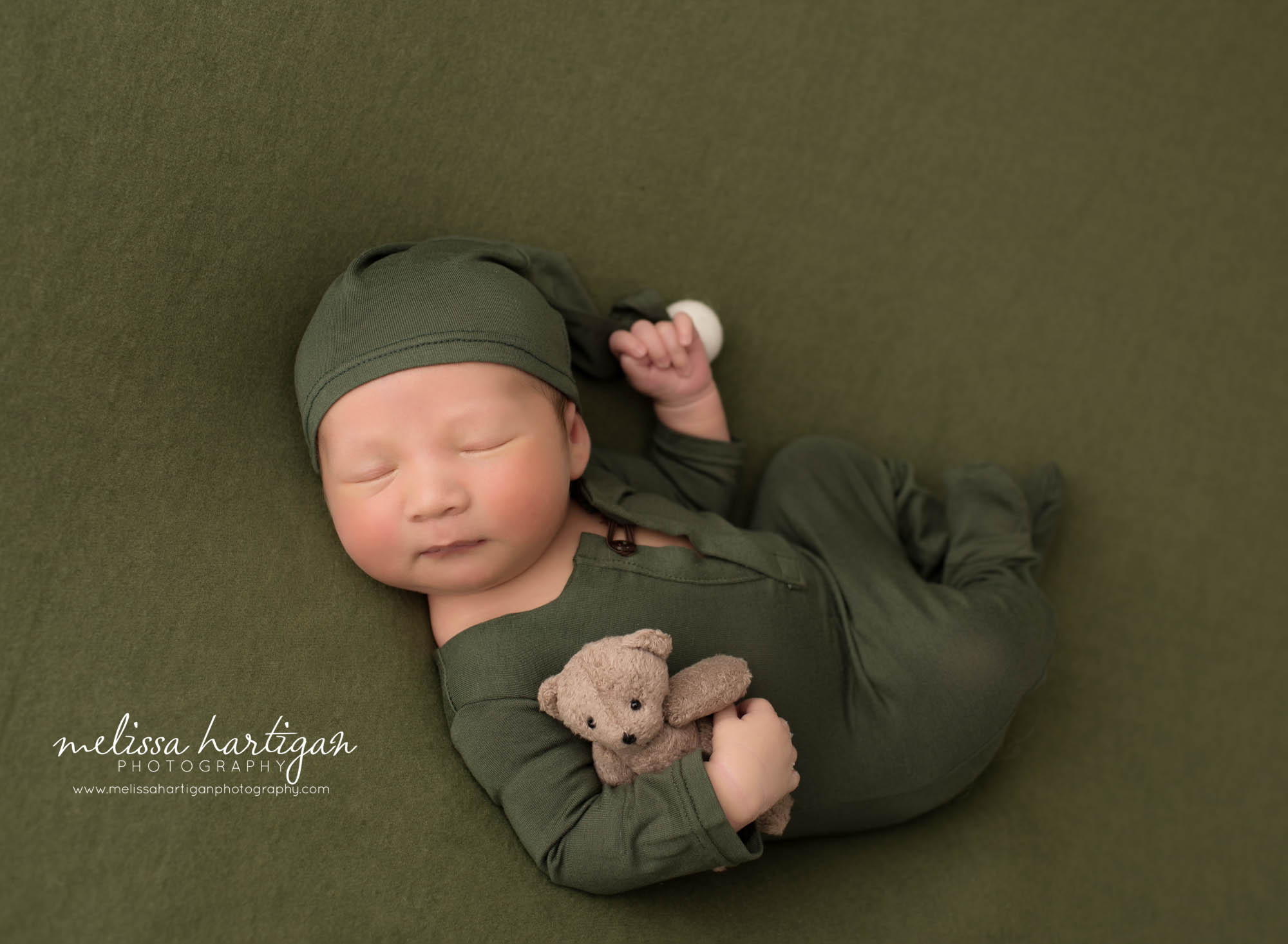 Newborn baby boy wearing green baby boy outfit with matching green sleepy cap posed with teddy bear prop Newborn Photography Ellington