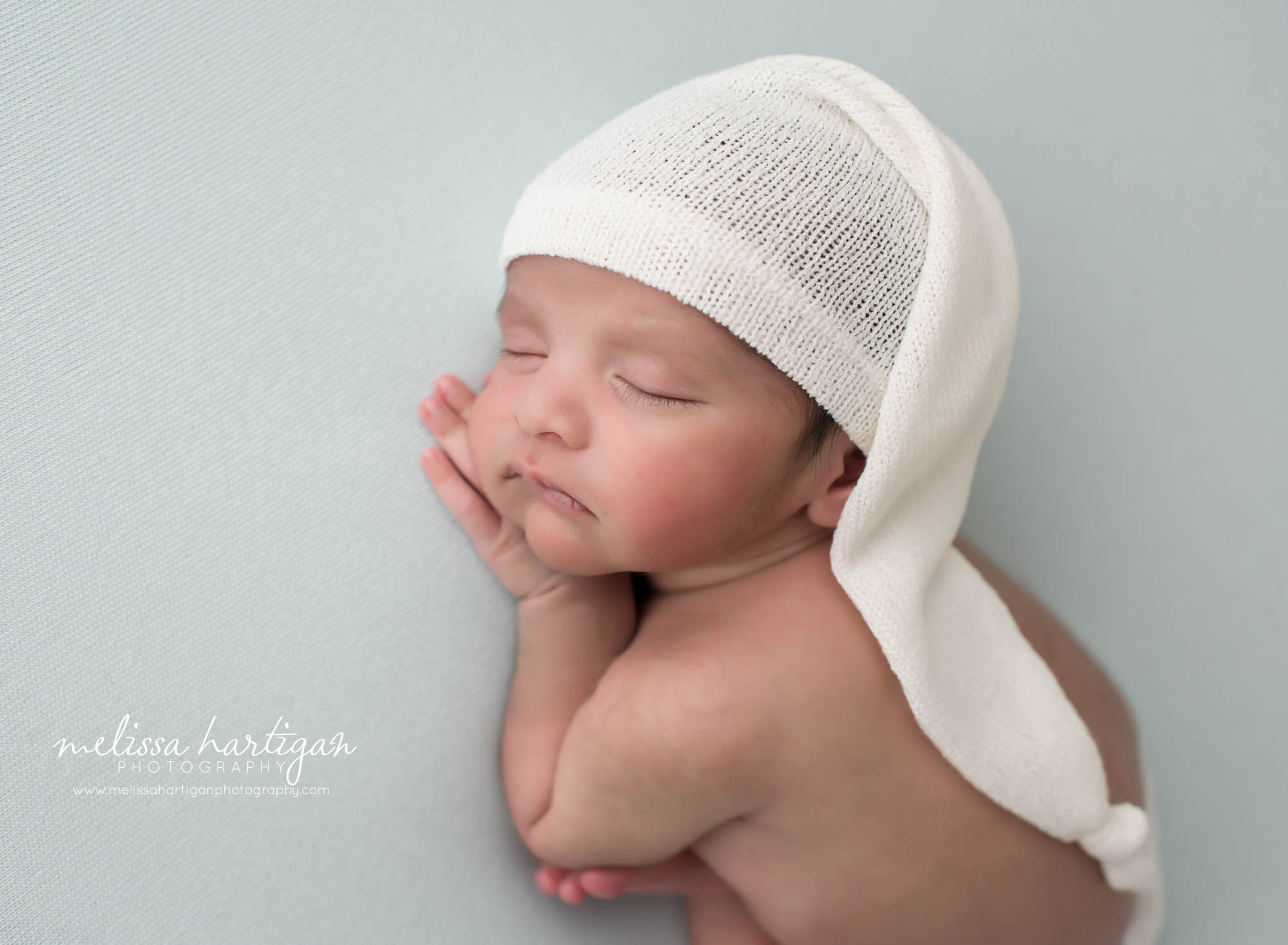 newborn baby boy posed on tummy with hand under cheek wearing cream knitted sleepy cap