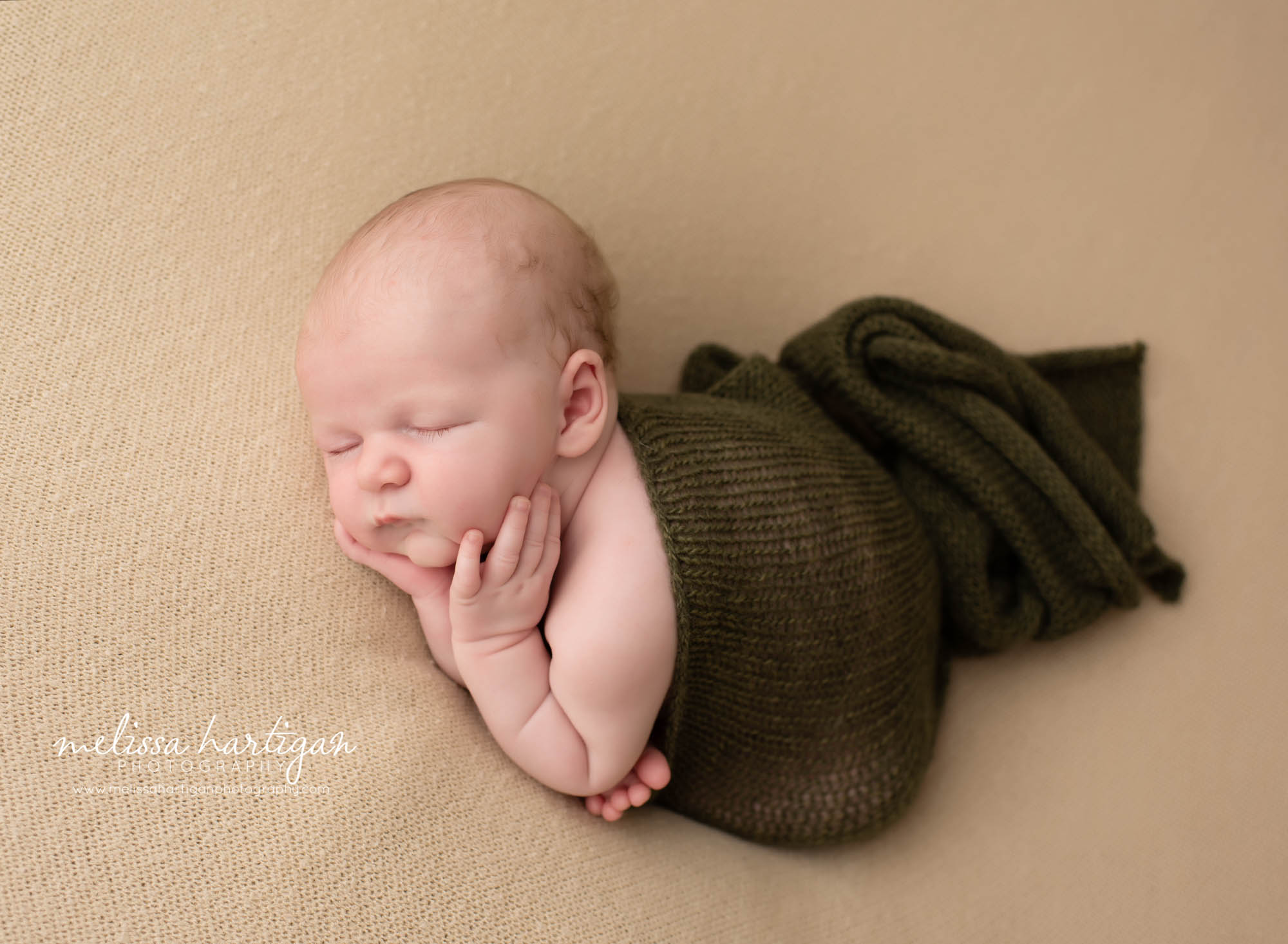 newborn baby boy posed on side with hands under chin draped with knitted green wrap