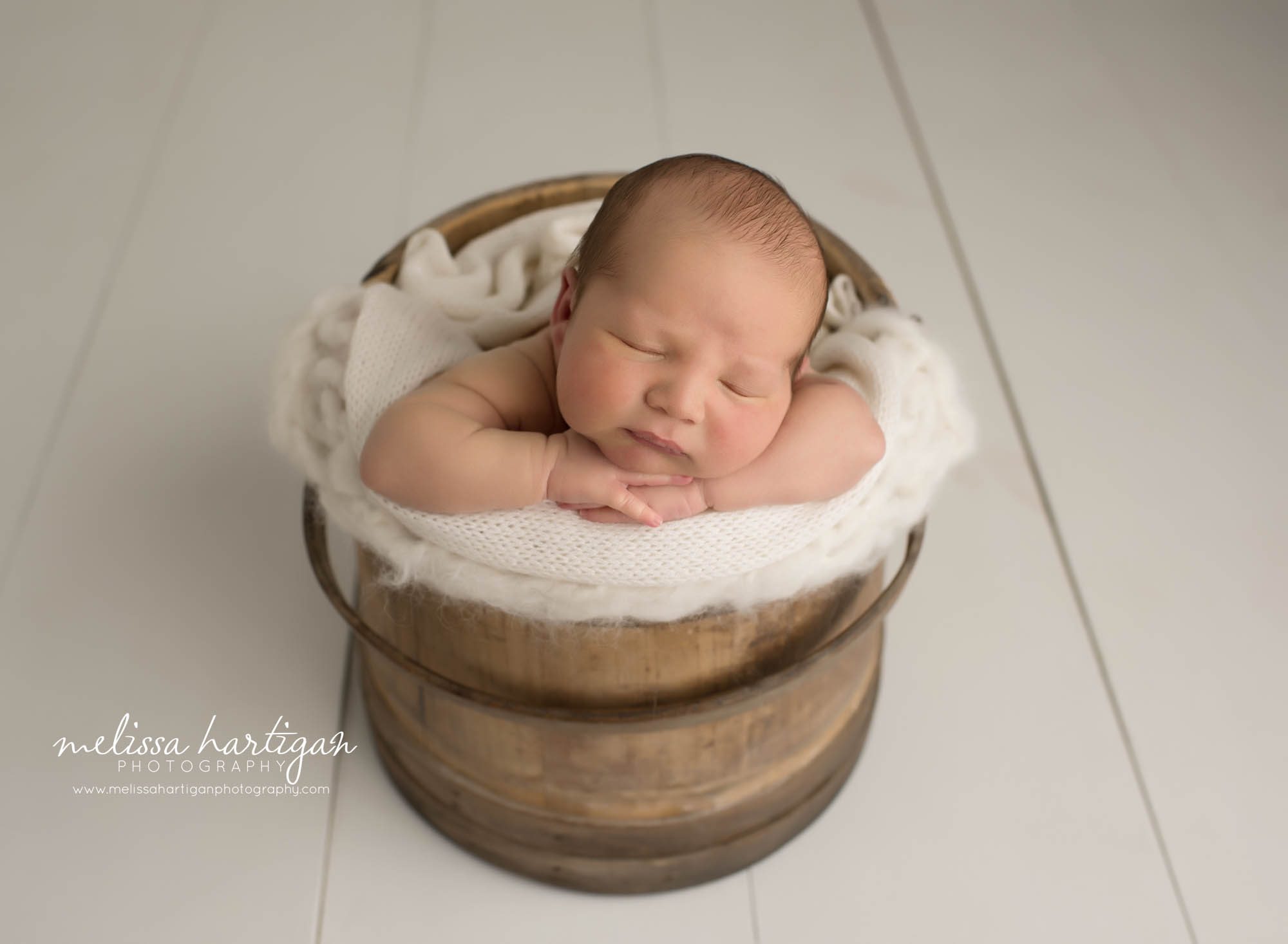 newborn baby boy posed in wooden barrel with cream layer wrap Newborn Photography Ellington