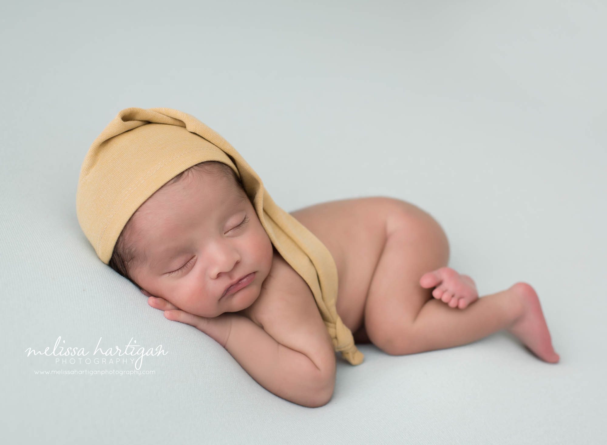 newborn baby boy posed on light blue backdrop wearing yellow sleepy cap glastonbury newborn photography