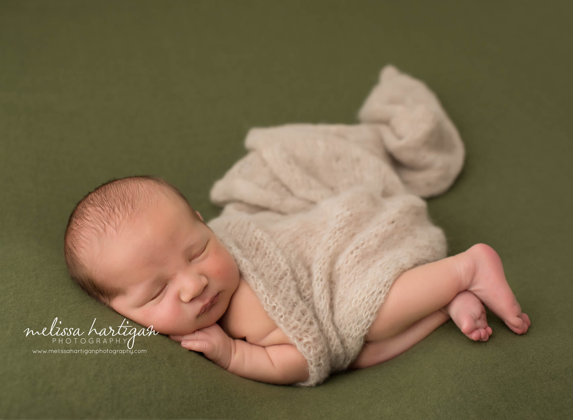 newborn baby boy posed on green backdrop with cream knit layer wrap