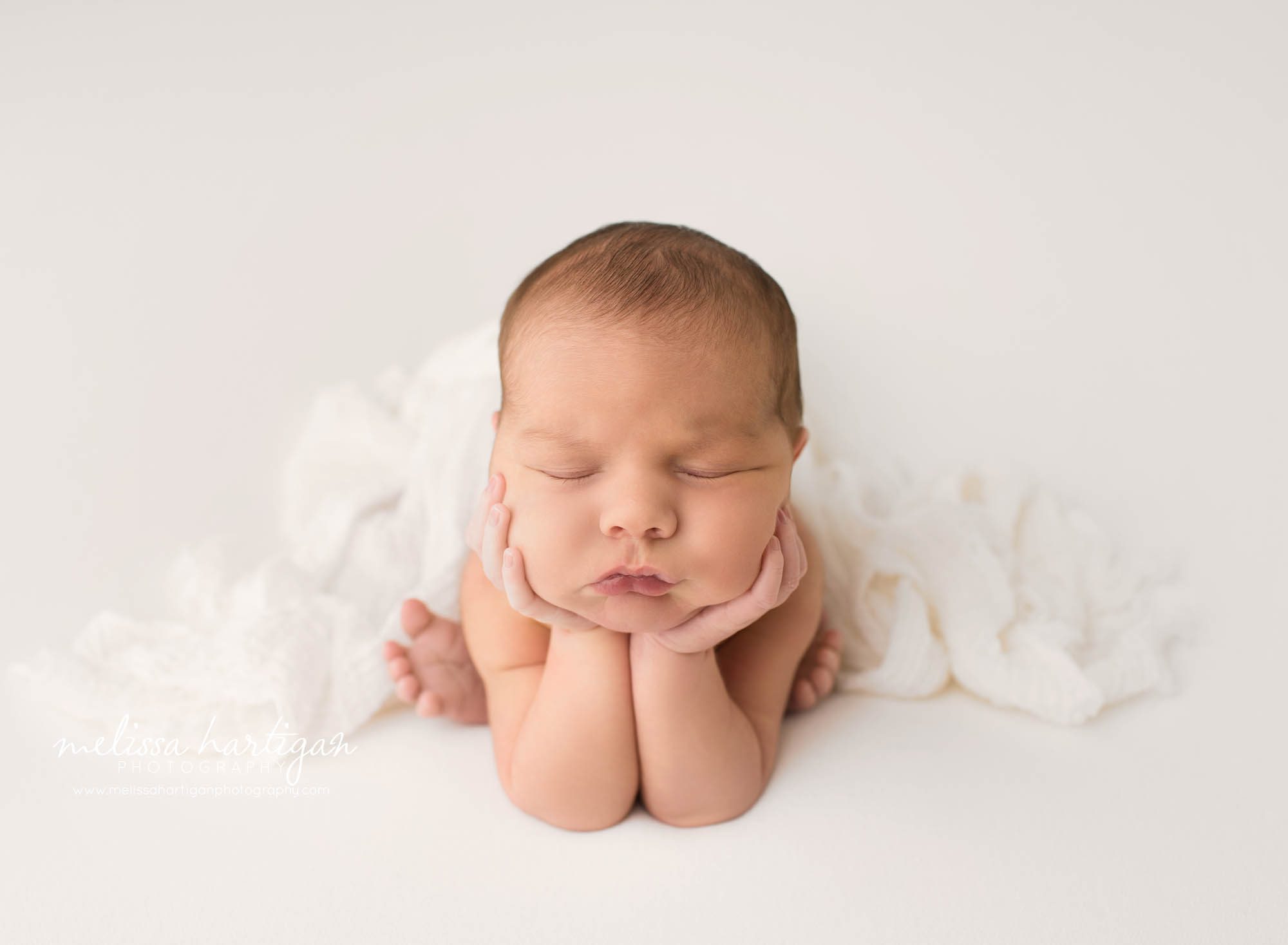 newborn baby boy posed froggy pose on white backdrop with white layer wrap drappd over baby photography windham county