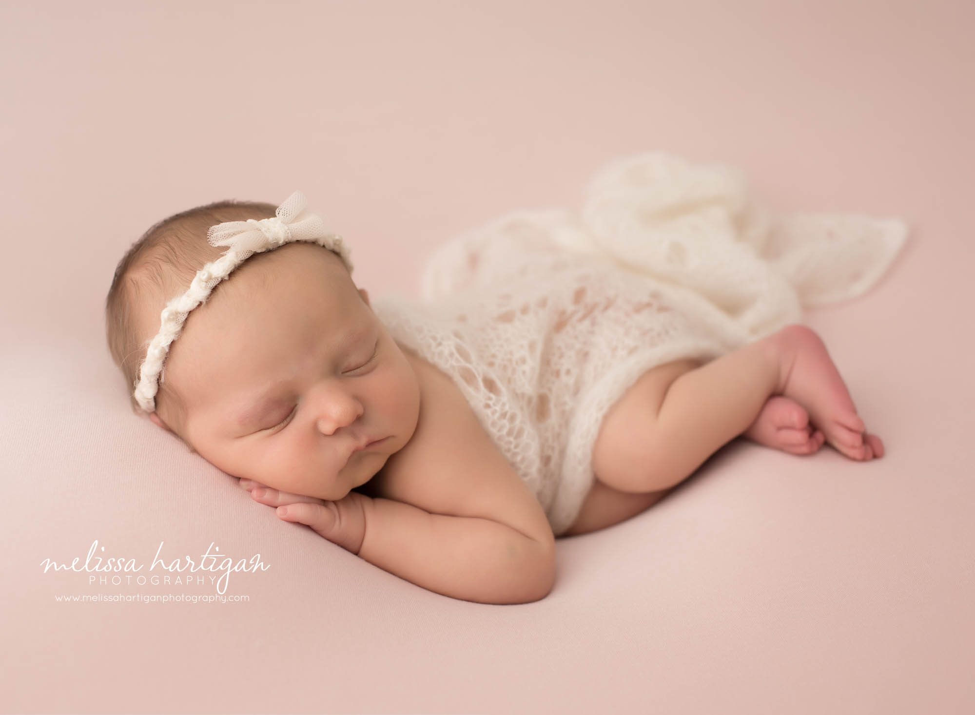 newborn baby girl posed on pink backdrop with cream knit wrap wearing bow headband