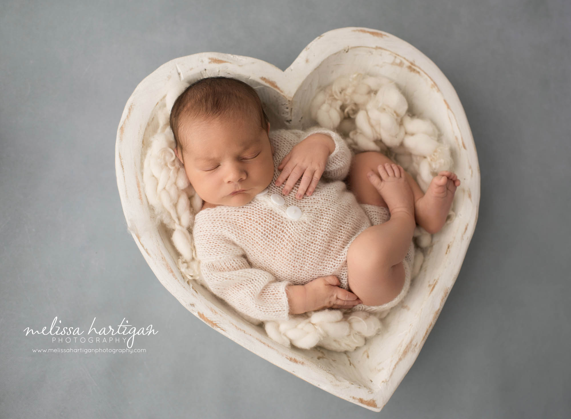 newborn baby boy posed in cream wooden heart shaped prop wearing knitted outfit newborn photography windham county ct