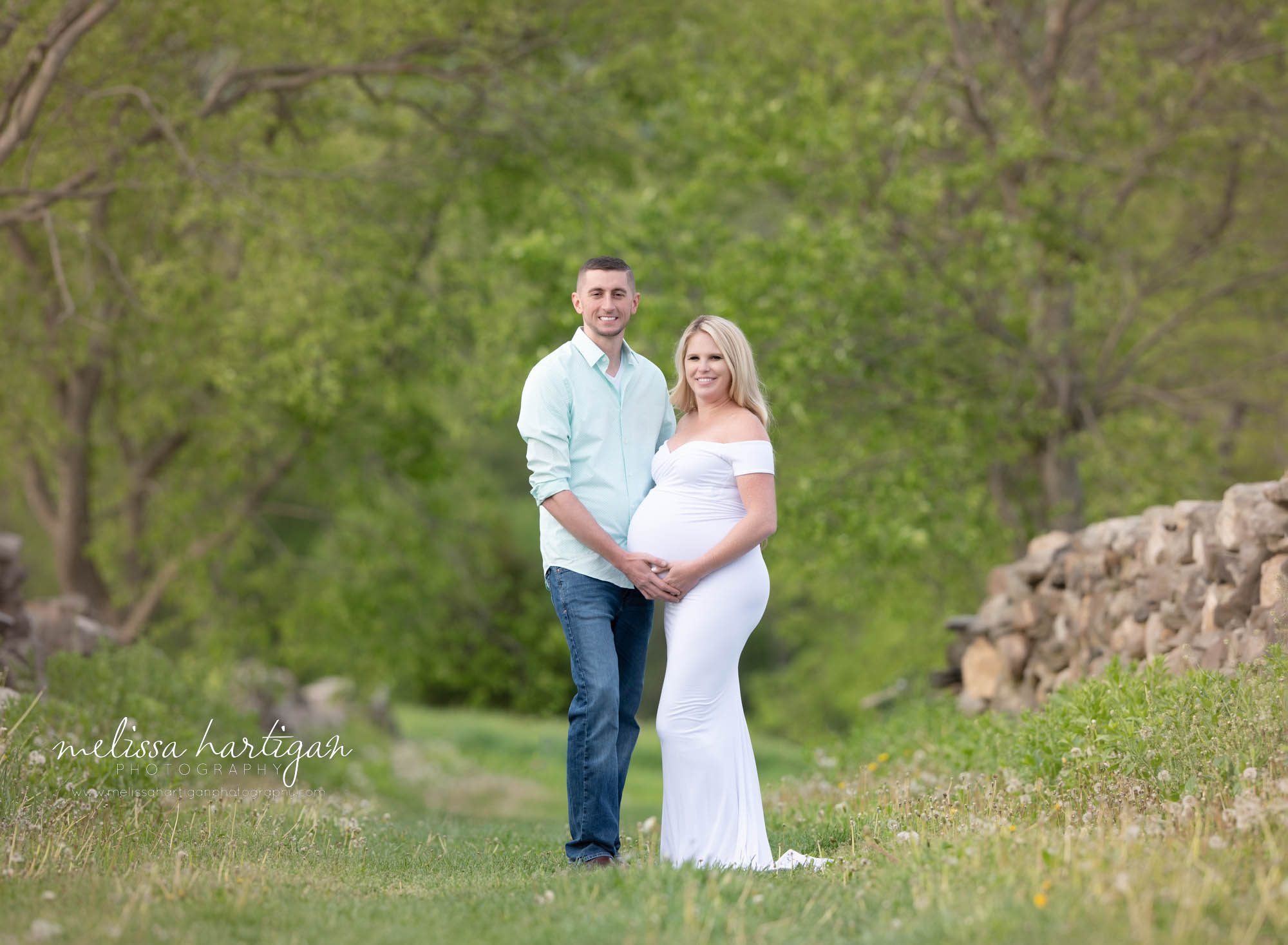 couple standing holding baby bump mom wearing white long form fitted maternity dress south windsor maternity photography
