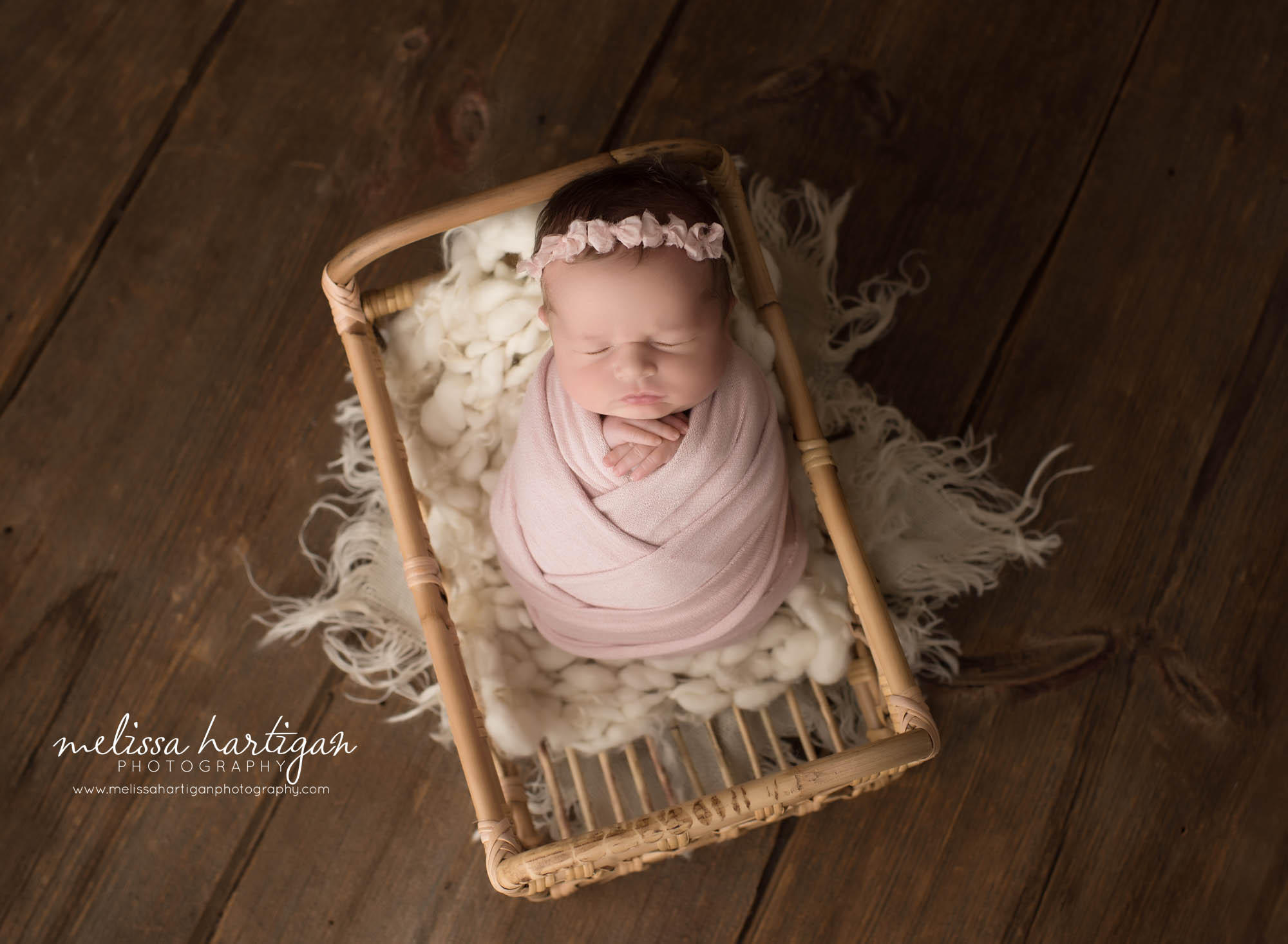 newborn baby girl posed on basket wrapped in pink wrap