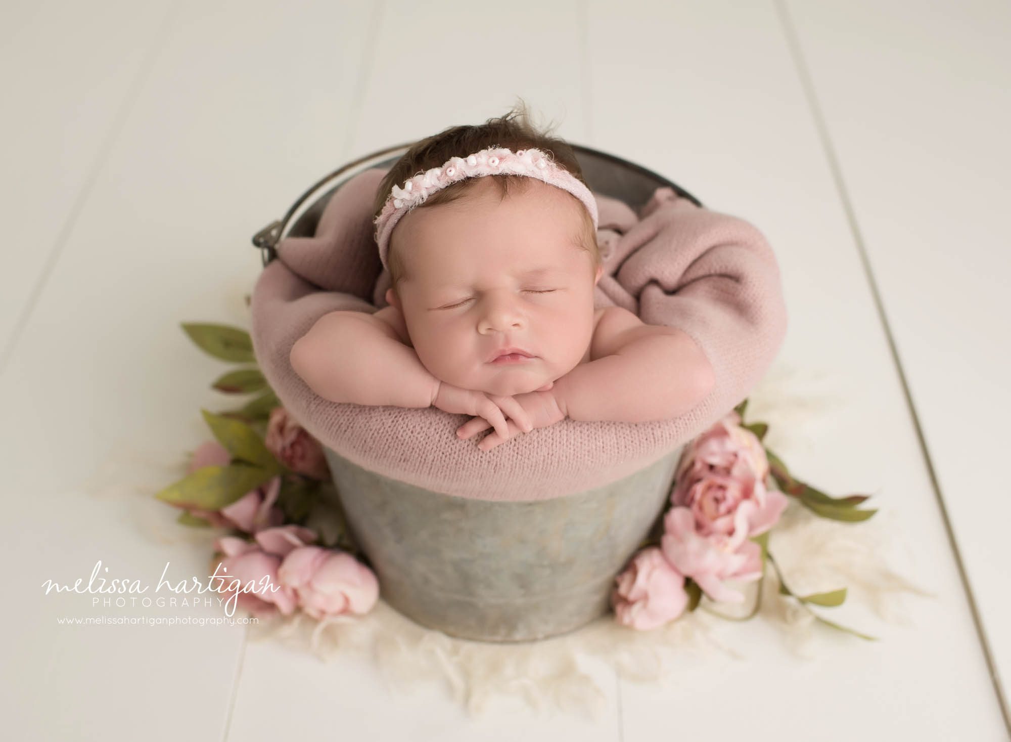 newborn baby girl posed in bucket with pink flowers and pink wrap ct newborn photography