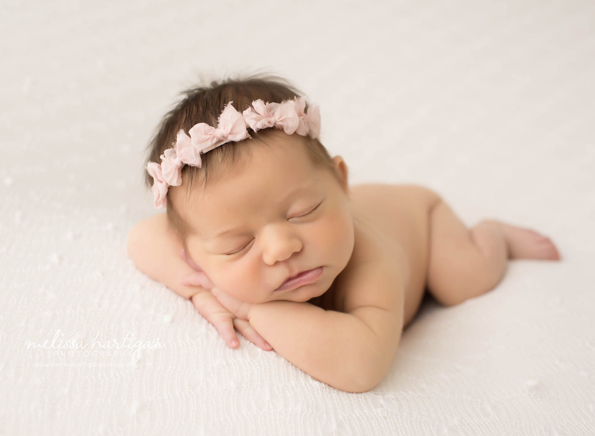 newborn baby girl posed with head on hands pose wearing pink bow headband