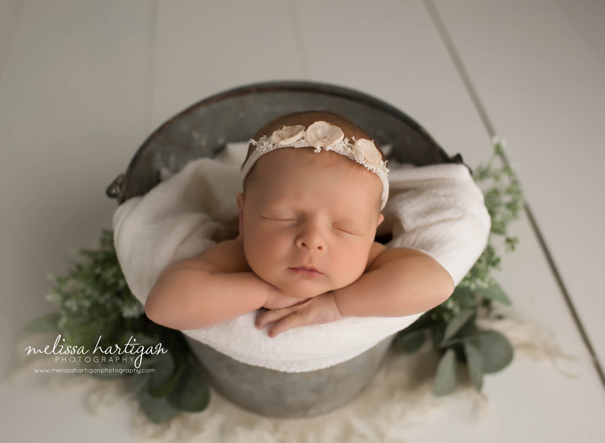 newborn baby girl posed in metal bucket with white wrap and floral headband