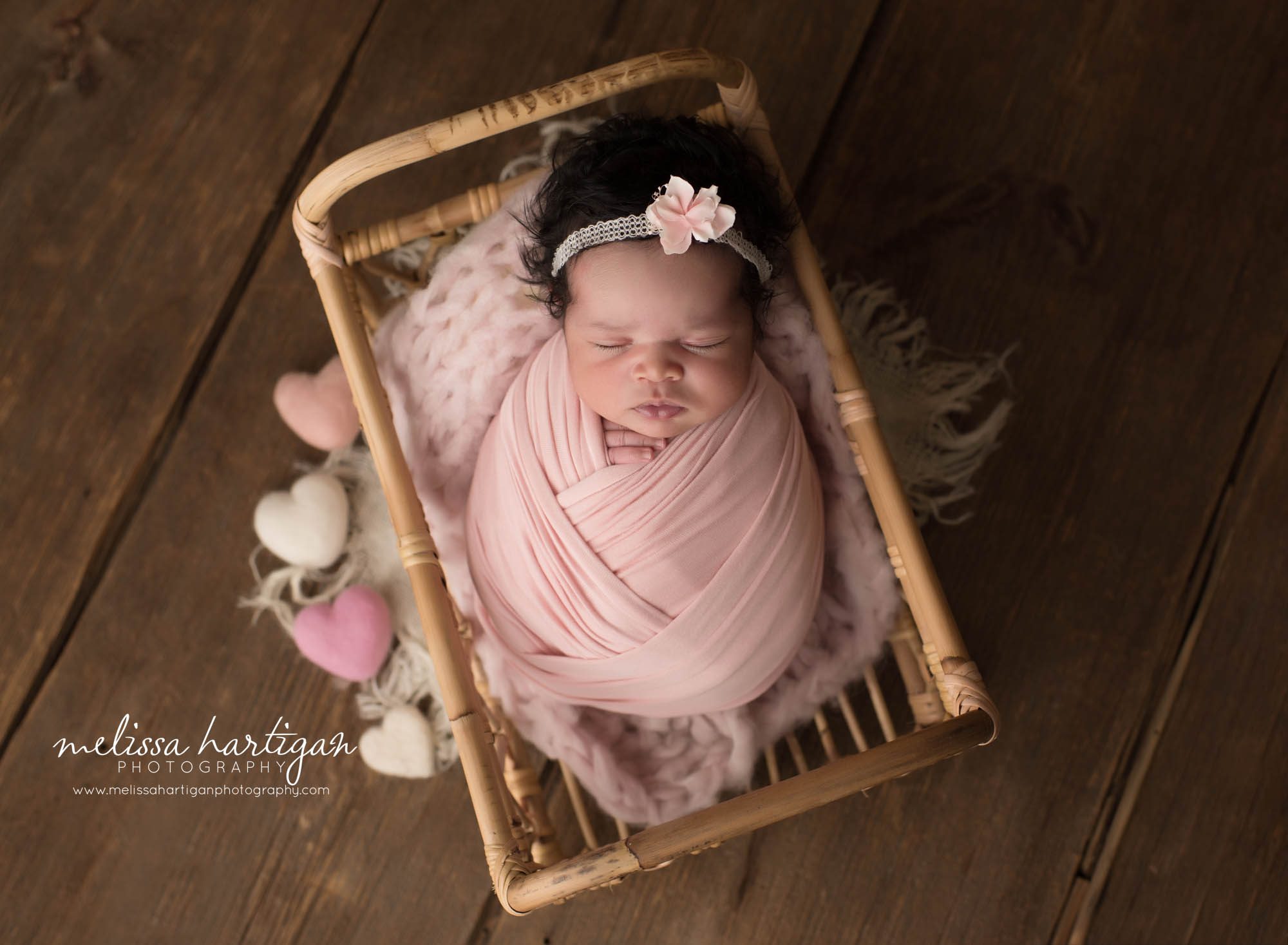 newborn baby girl wrapped in ink wrap posed in basket with pink and cream hearts